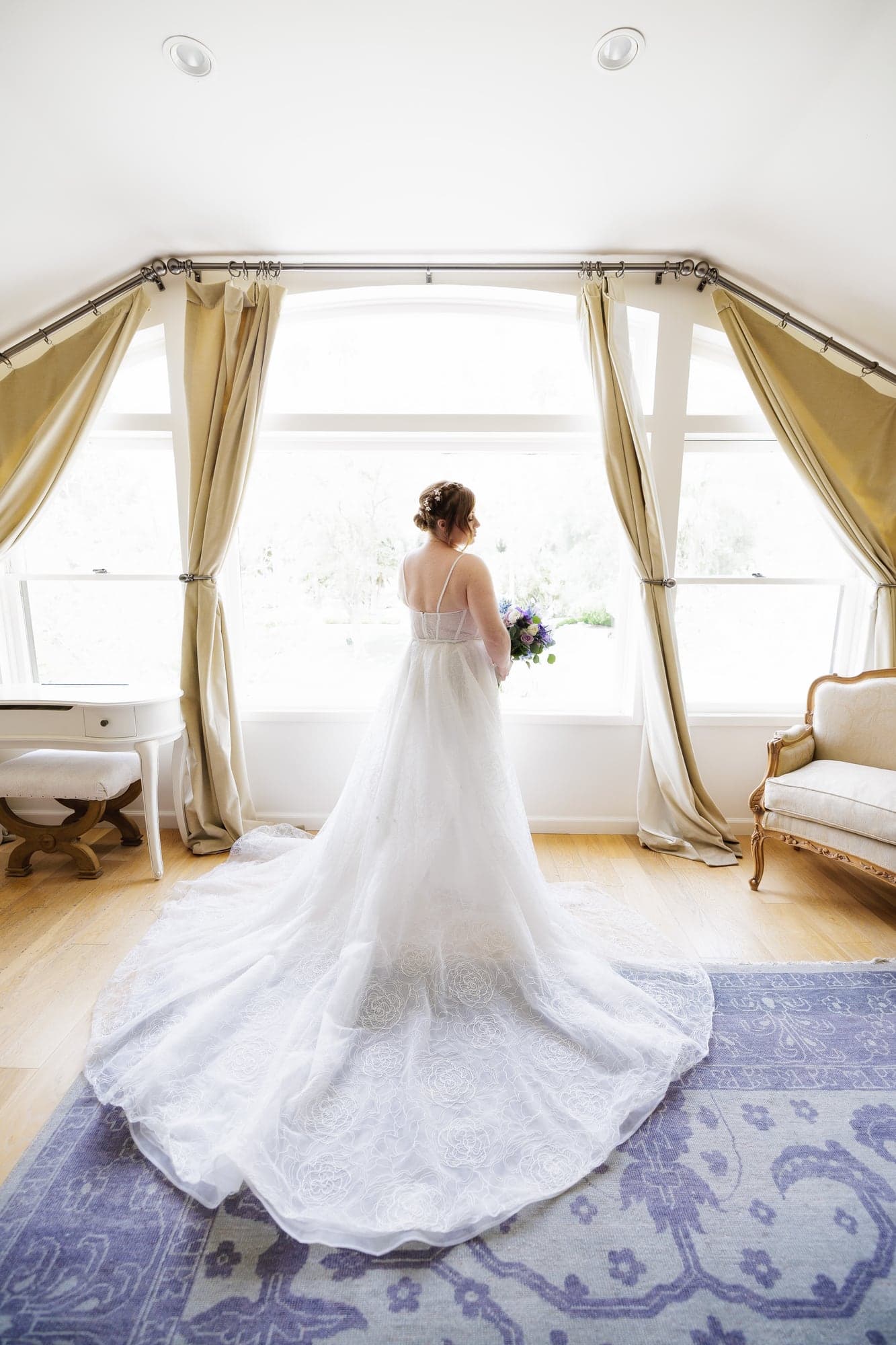Rachel standing in a bright Newhall Mansion room with her wedding train spread behind her