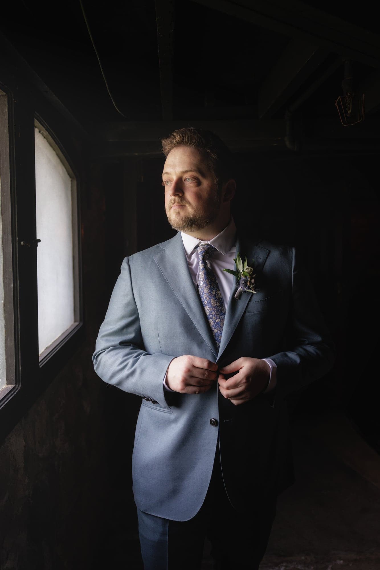 Travis standing in formalwear beside a narrow window inside Newhall Mansion