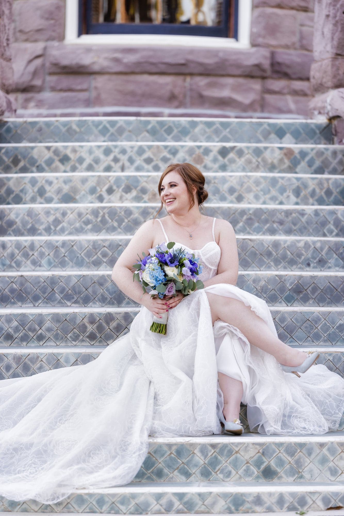 Rachel seated with her wedding gown flowing down Newhall Mansion's stone staircase