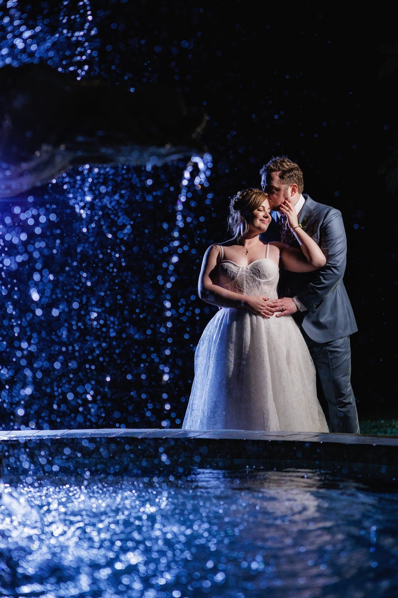 Rachel and Travis standing together beneath blue nighttime garden lights at Newhall Mansion