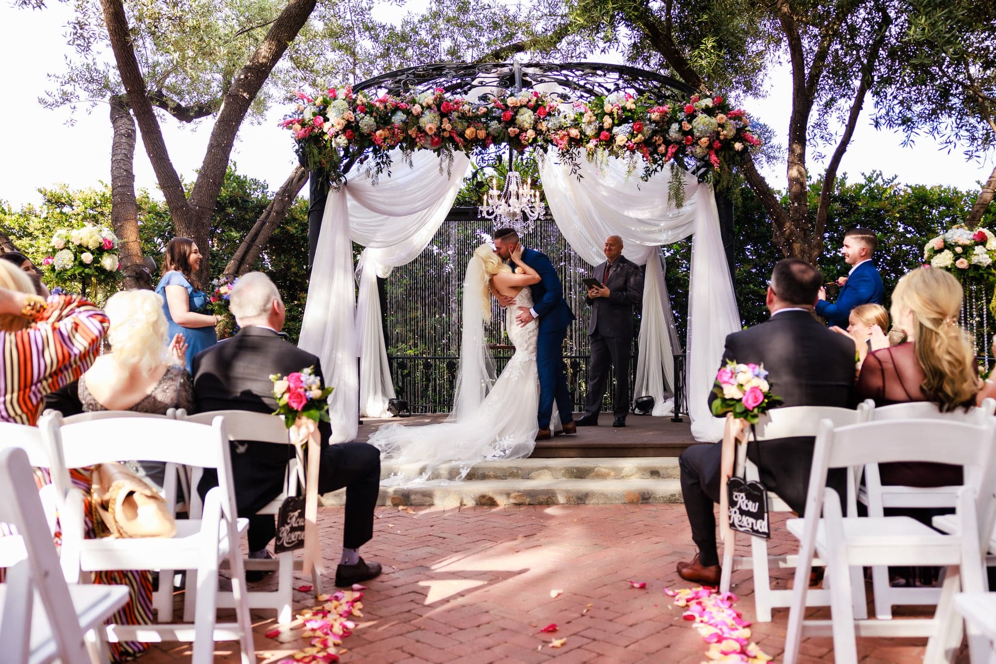 Mary and Tyler exchanging vows beneath a flower-covered arch at Padua Hills Theatre