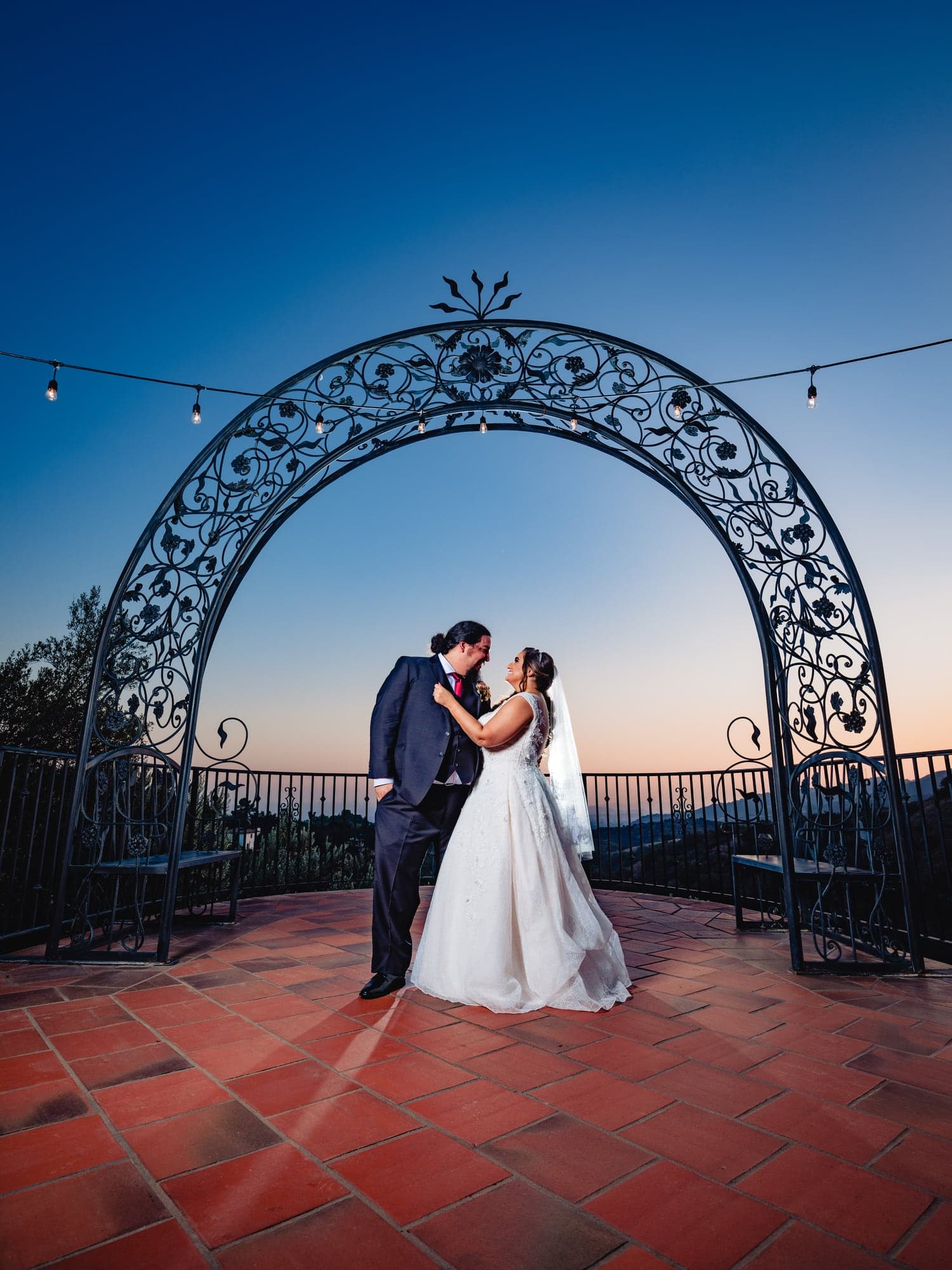 Nareen and Jesse beneath a wrought-iron arch at dusk