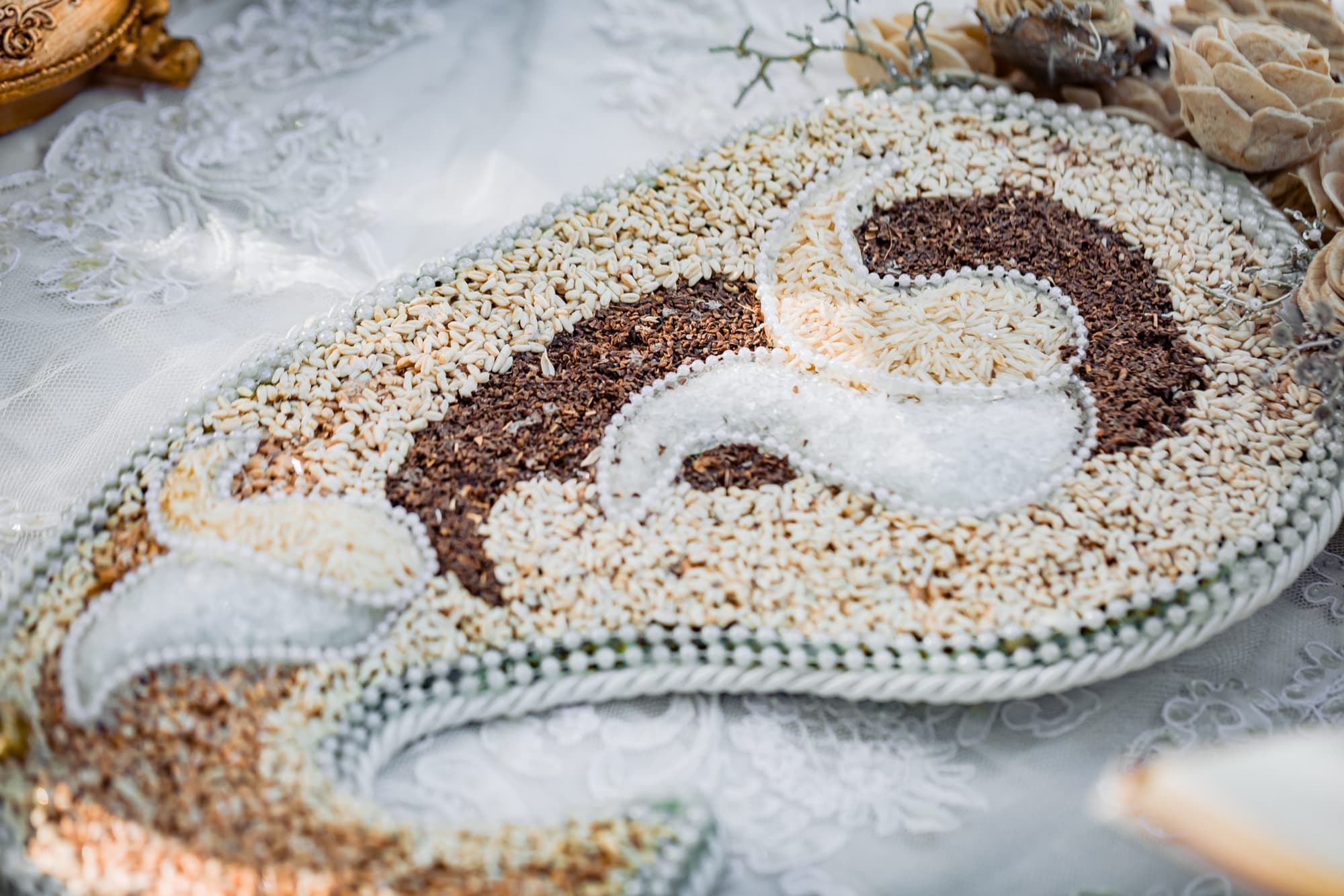 Decorated flatbread on the sofreh aghd with seeds arranged in a paisley pattern beside lace and pearls