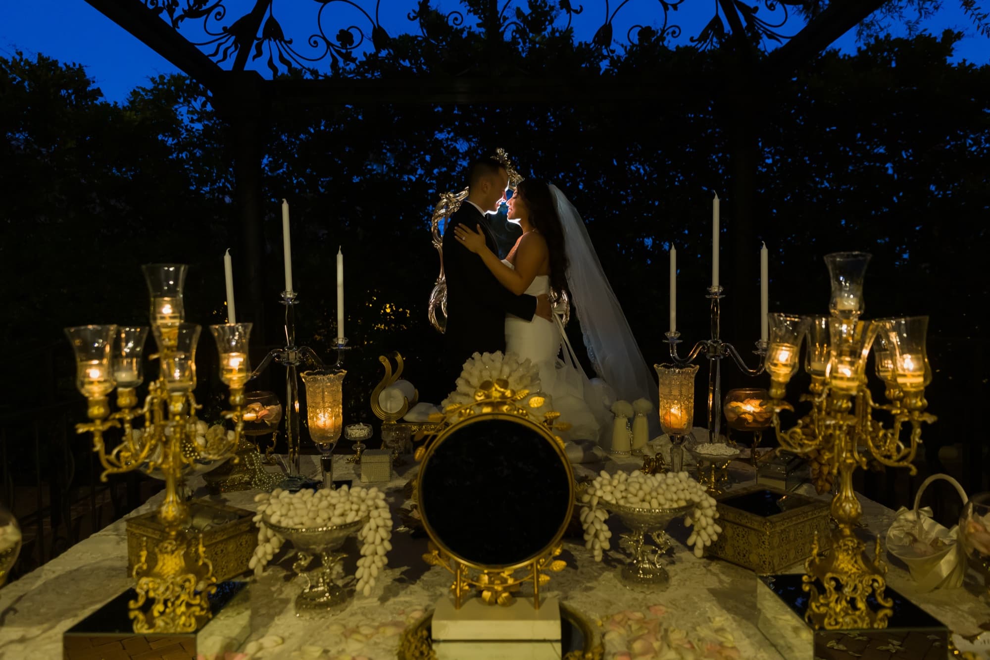 Soraya and Donald kissing at their candlelit sofreh aghd at night at Padua Hills Theatre, gold candelabras and the ceremonial mirror glowing around them, photographed by Michael Anthony Photography