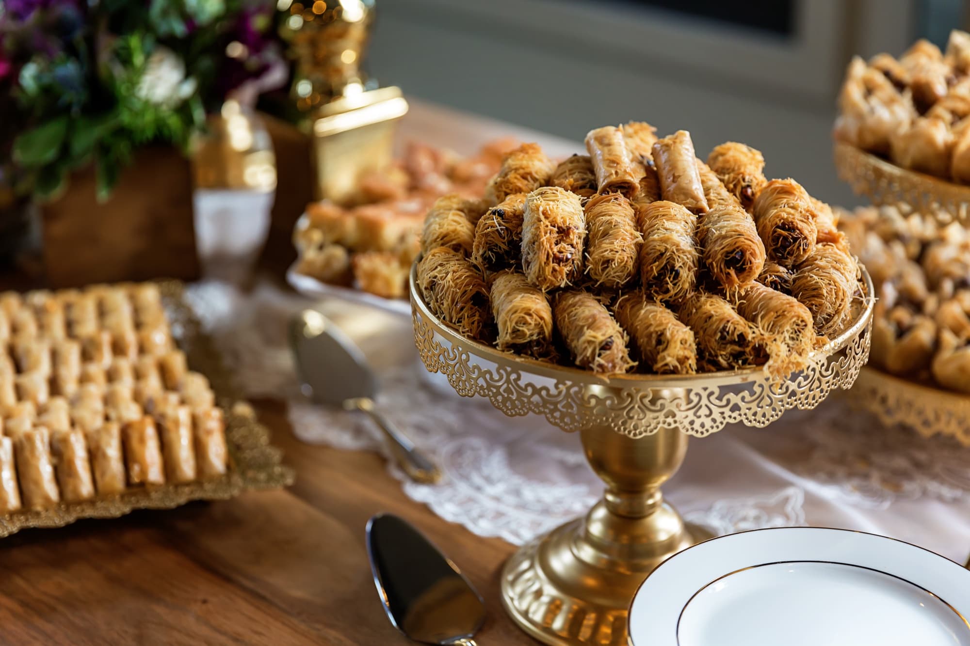 Gold cake stands stacked with baklava and kunafa on the dessert table at Yomna and Bradley's reception