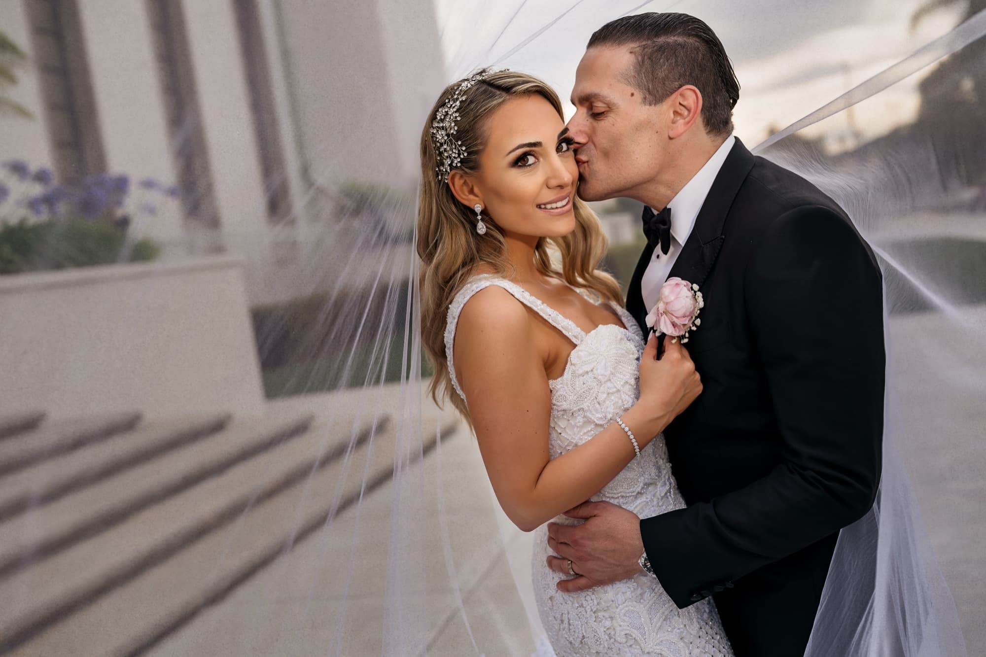 Garen kissing Laura's cheek as her veil wraps around them both outside the cathedral
