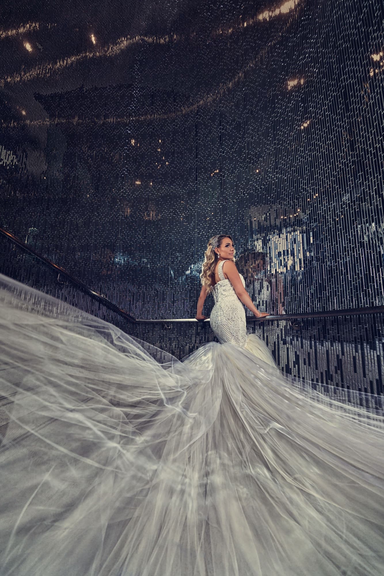 Laura on the staircase at Vertigo Event Venue with her mermaid train cascading down the steps against the glass-mosaic wall