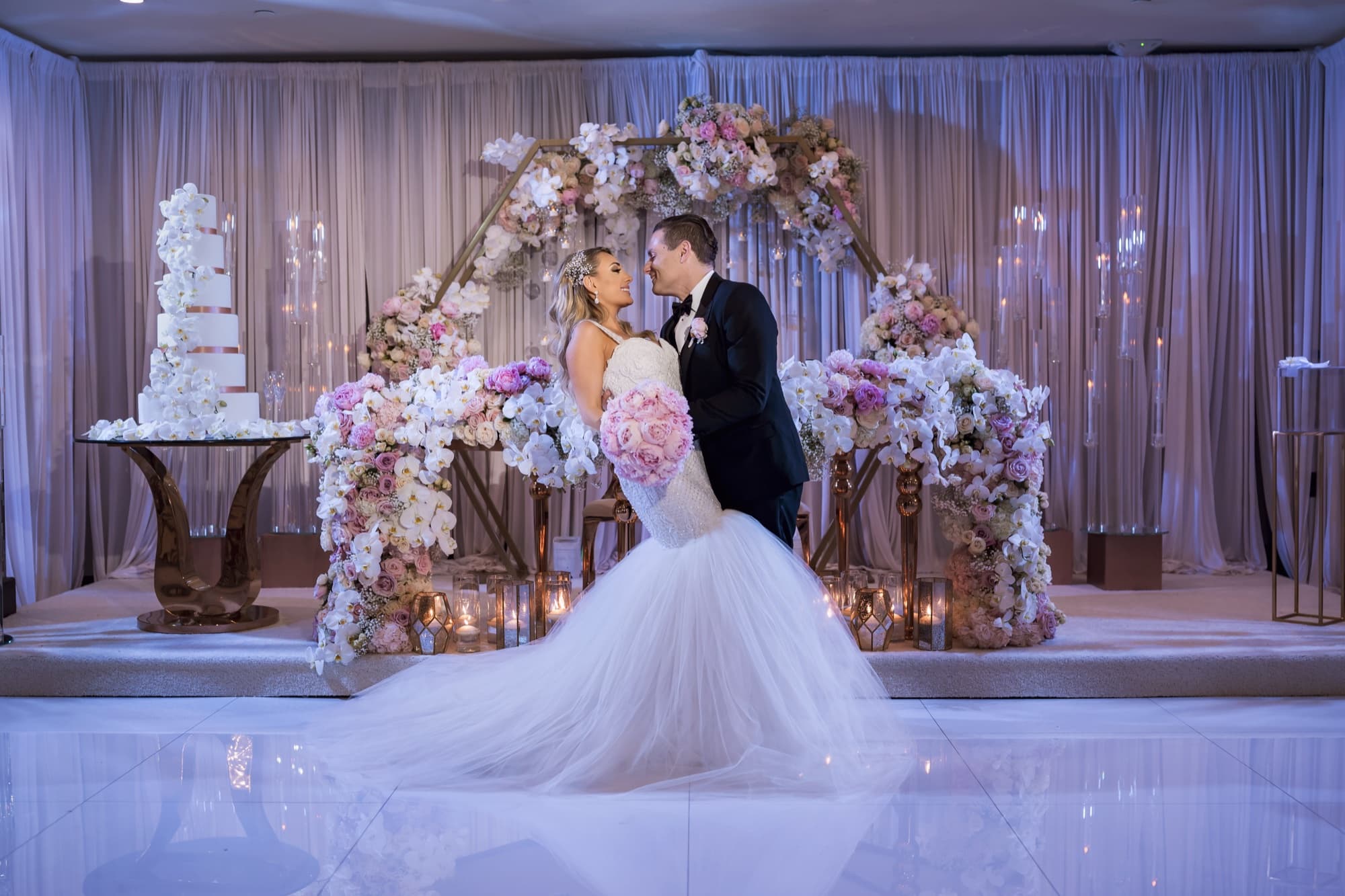 Laura and Garen on the sweetheart stage at Vertigo surrounded by blush florals, candles, and their blossom-wrapped cake