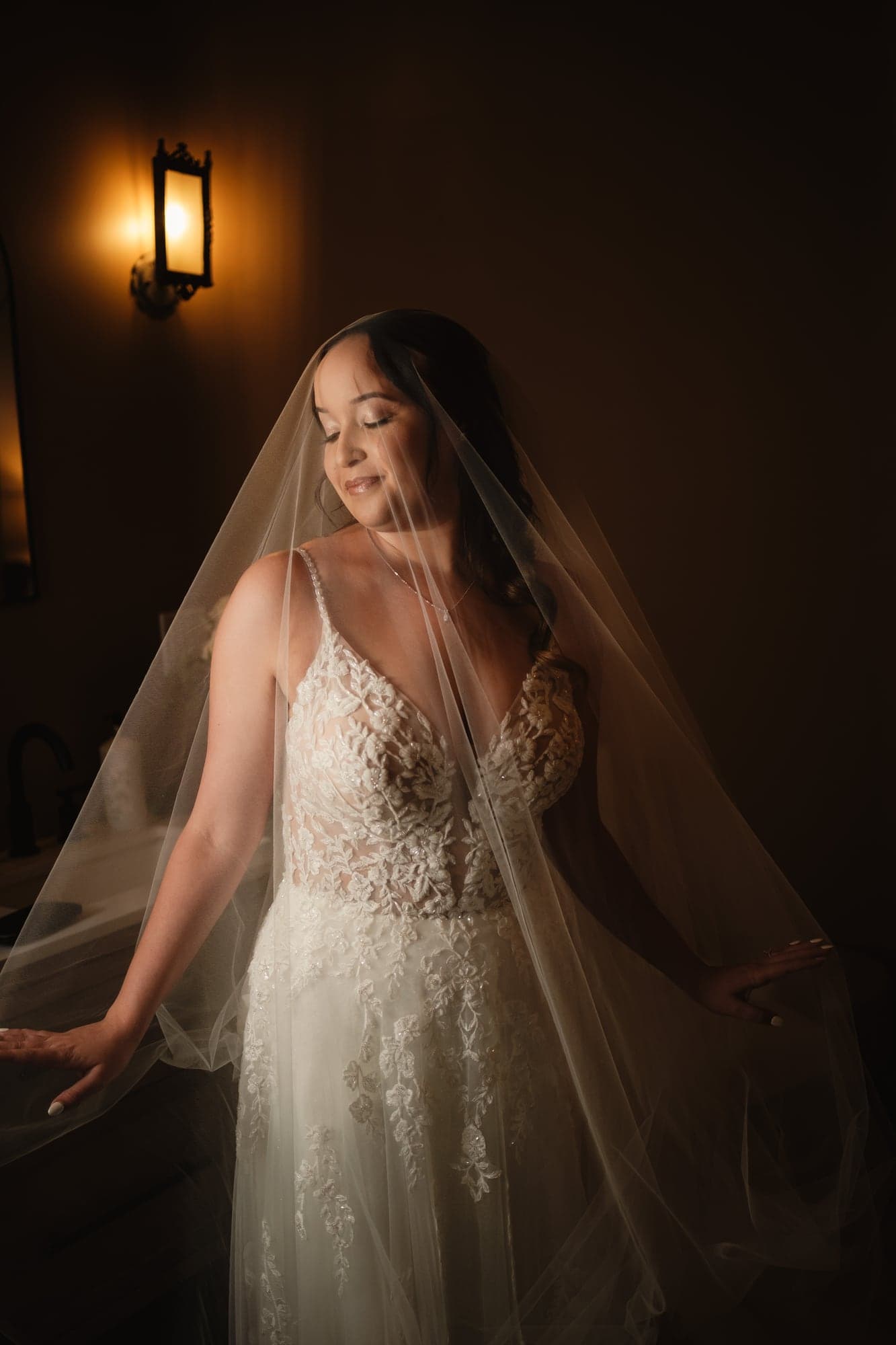 Leslie standing in warm window light beneath her veil