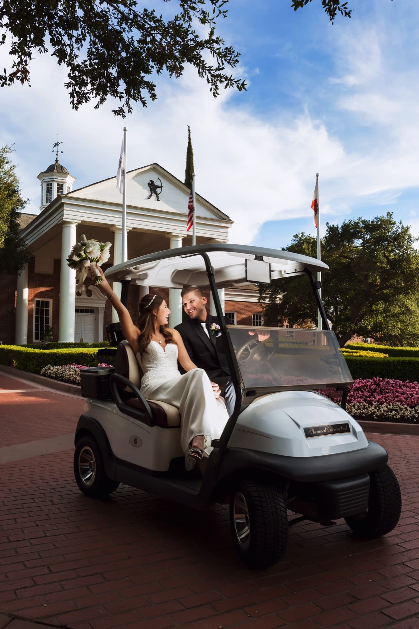 Heather and Brandon riding a golf cart through the Sherwood grounds with her bouquet raised in celebration