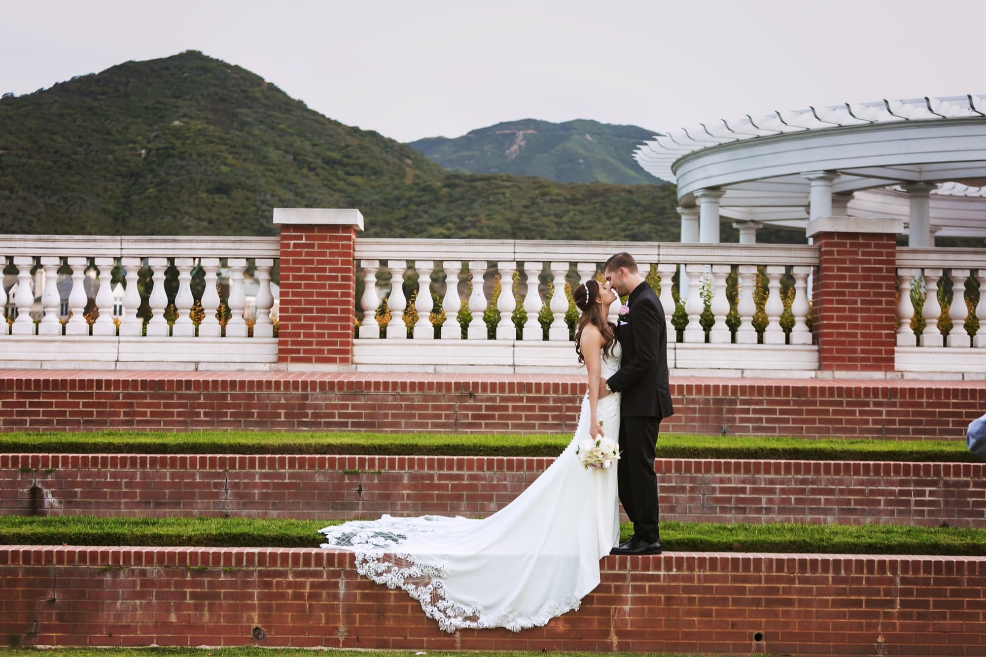 Heather and Brandon kissing on the brick terrace steps with her train cascading down and the rotunda in the distance