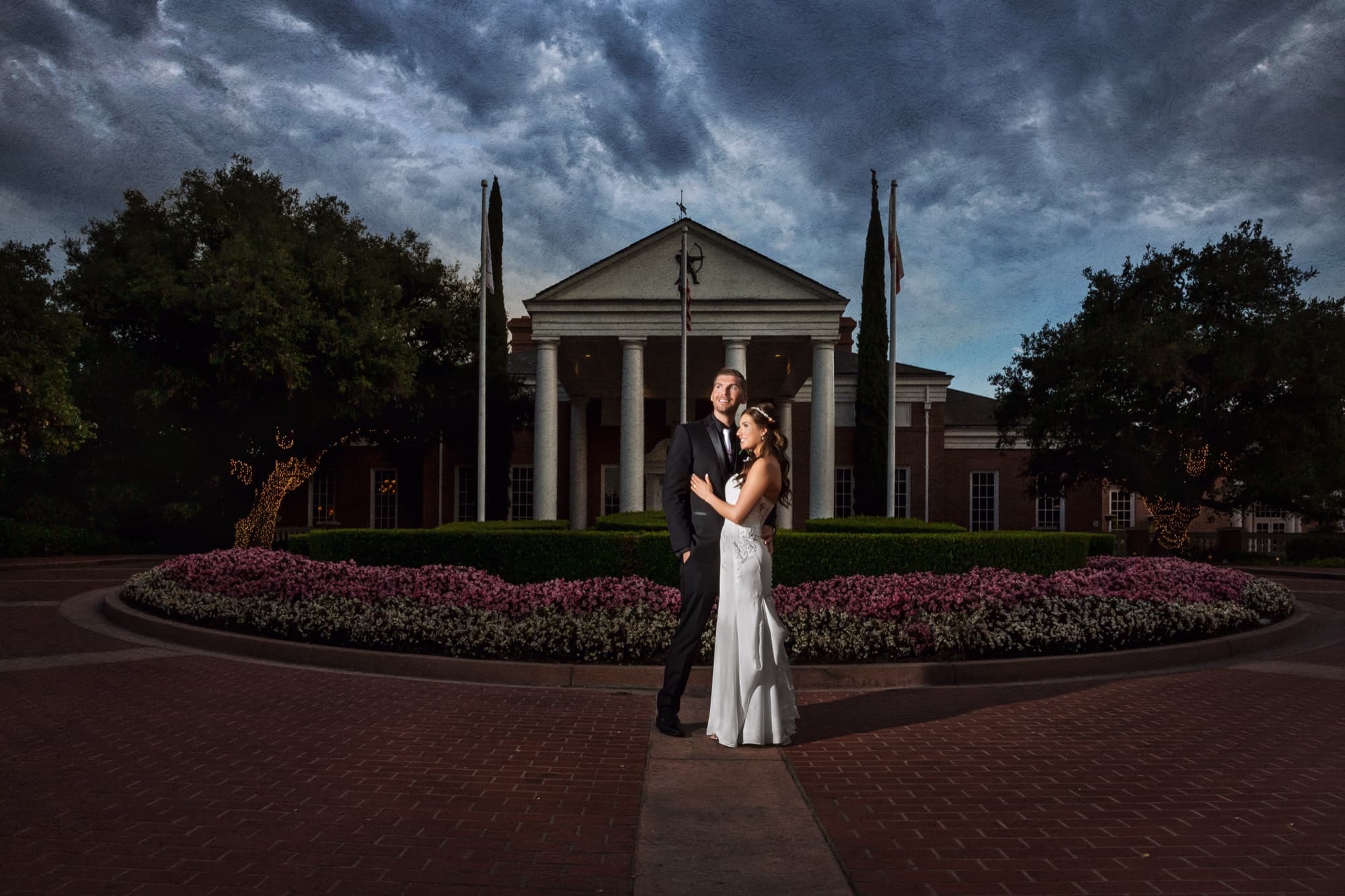 Heather and Brandon in the motor court at dusk with the columned Sherwood clubhouse under a dramatic storm sky