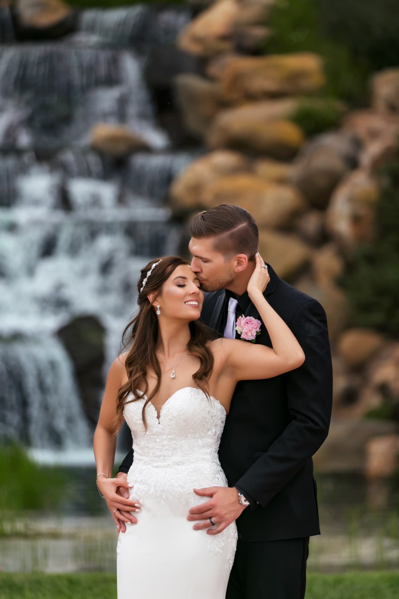 Brandon kissing Heather's forehead in front of the waterfall at Sherwood Country Club, photographed by Michael Anthony Photography