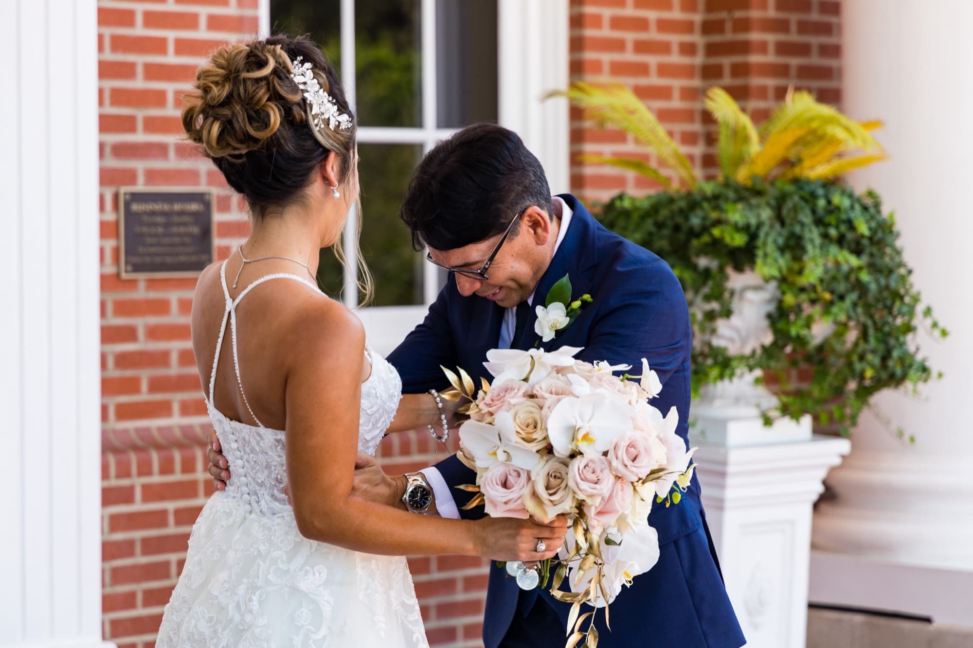 Groom in a navy suit reaching for the bride during their first look on the brick portico at Sherwood Country Club in Thousand Oaks