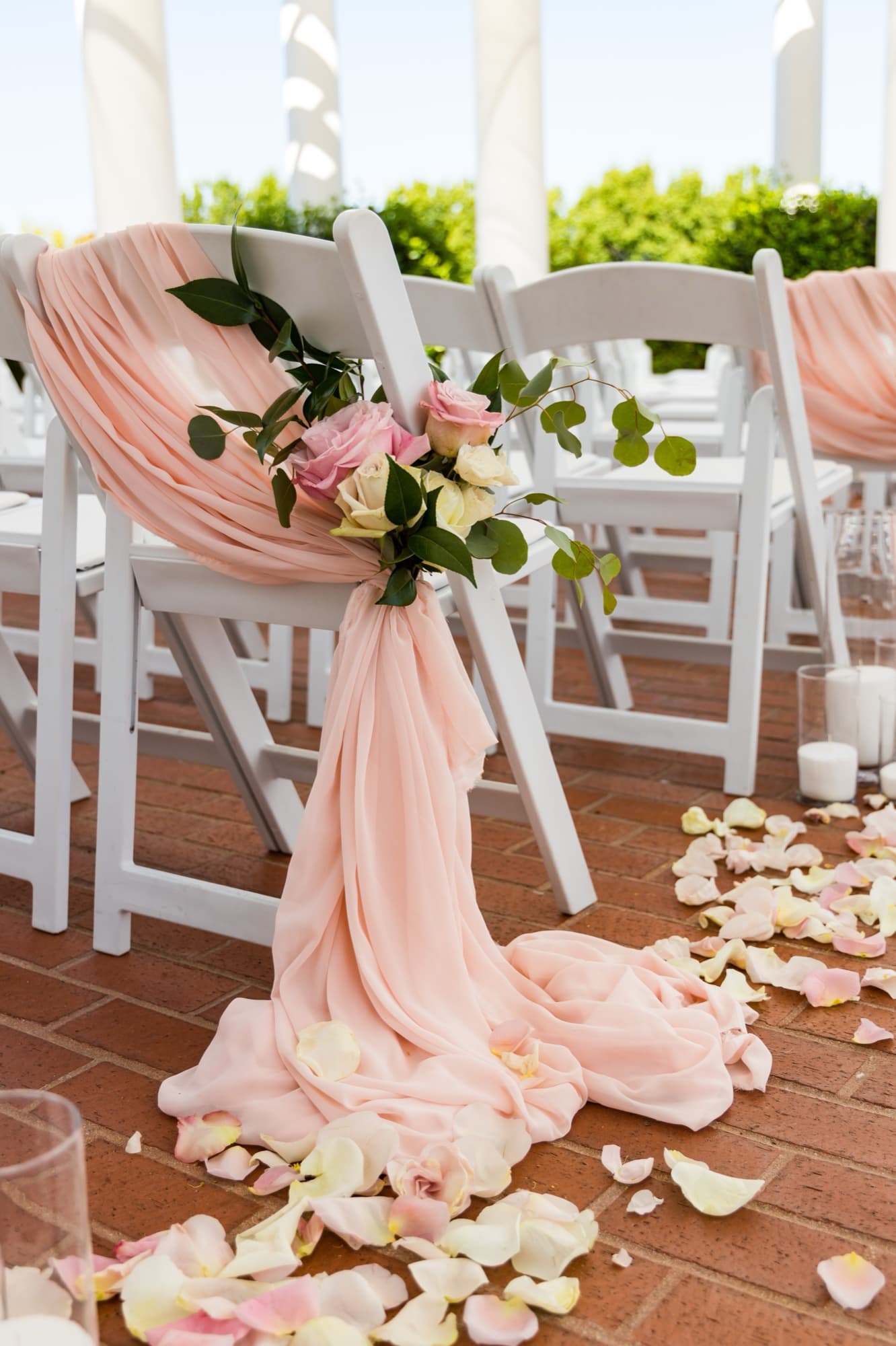 White folding ceremony chair wrapped in blush chiffon and roses with petals scattered on the brick aisle at a Sherwood Country Club wedding ceremony