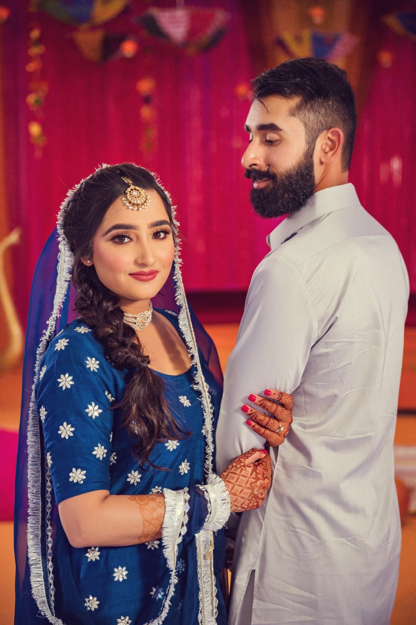 Harmen in a royal blue suit with fresh mehndi standing with Amaritpal in a white kurta at their sangeet