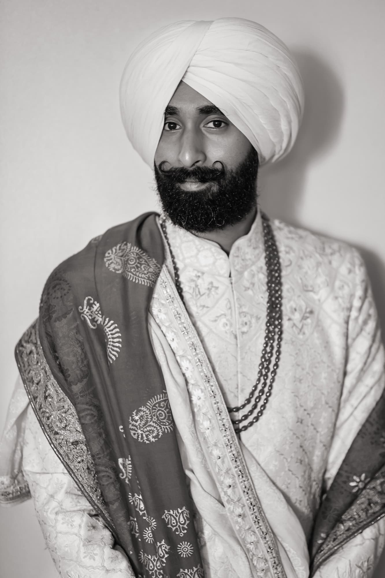Black and white portrait of Amaritpal in his turban and ivory sherwani with layered pearl necklaces