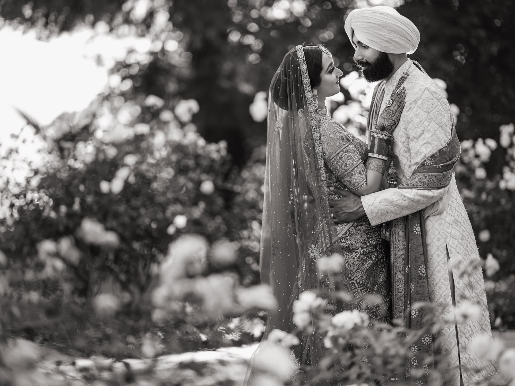Black and white photograph of Amaritpal dipping Harmen for a kiss among the roses