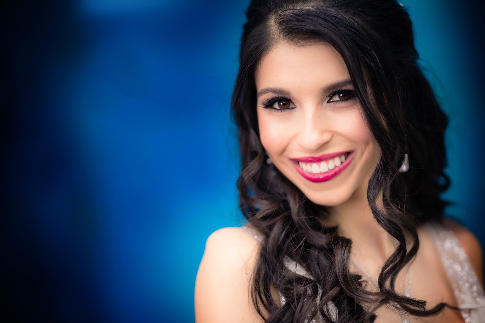 Beauty portrait of Rachel with long dark curls and red lips against a deep blue background