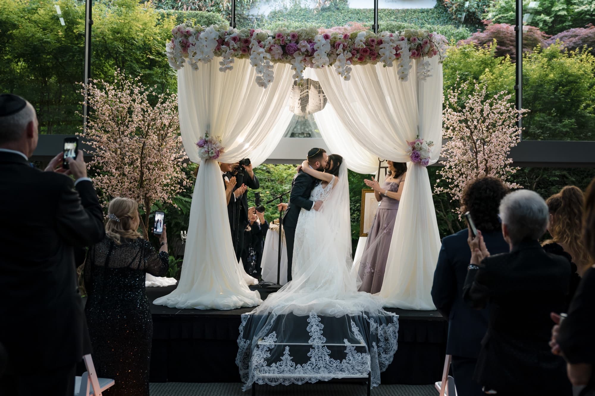 Rachel and Jeff embracing beneath the chuppah as guests photograph the moment at the Skirball Cultural Center