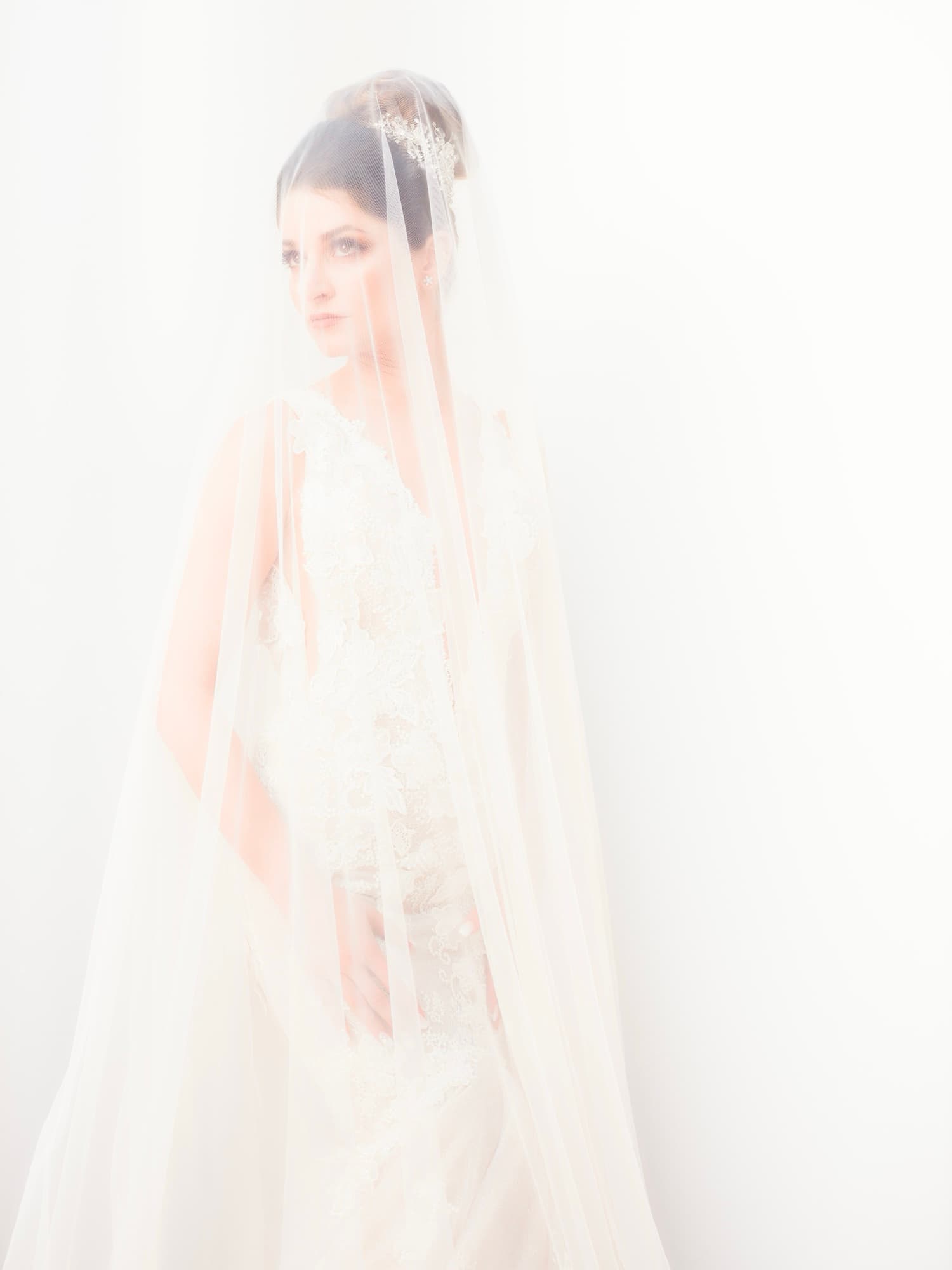 High-key bridal portrait of Yana beneath her veil in the bright white suite light