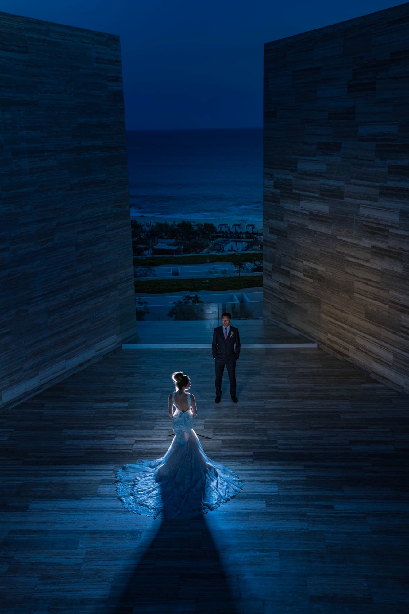 Yana and Jonathan at blue hour in the monolithic stone corridor at Solaz Los Cabos, her train glowing as the corridor frames the Sea of Cortez behind them, photographed by Michael Anthony Photography