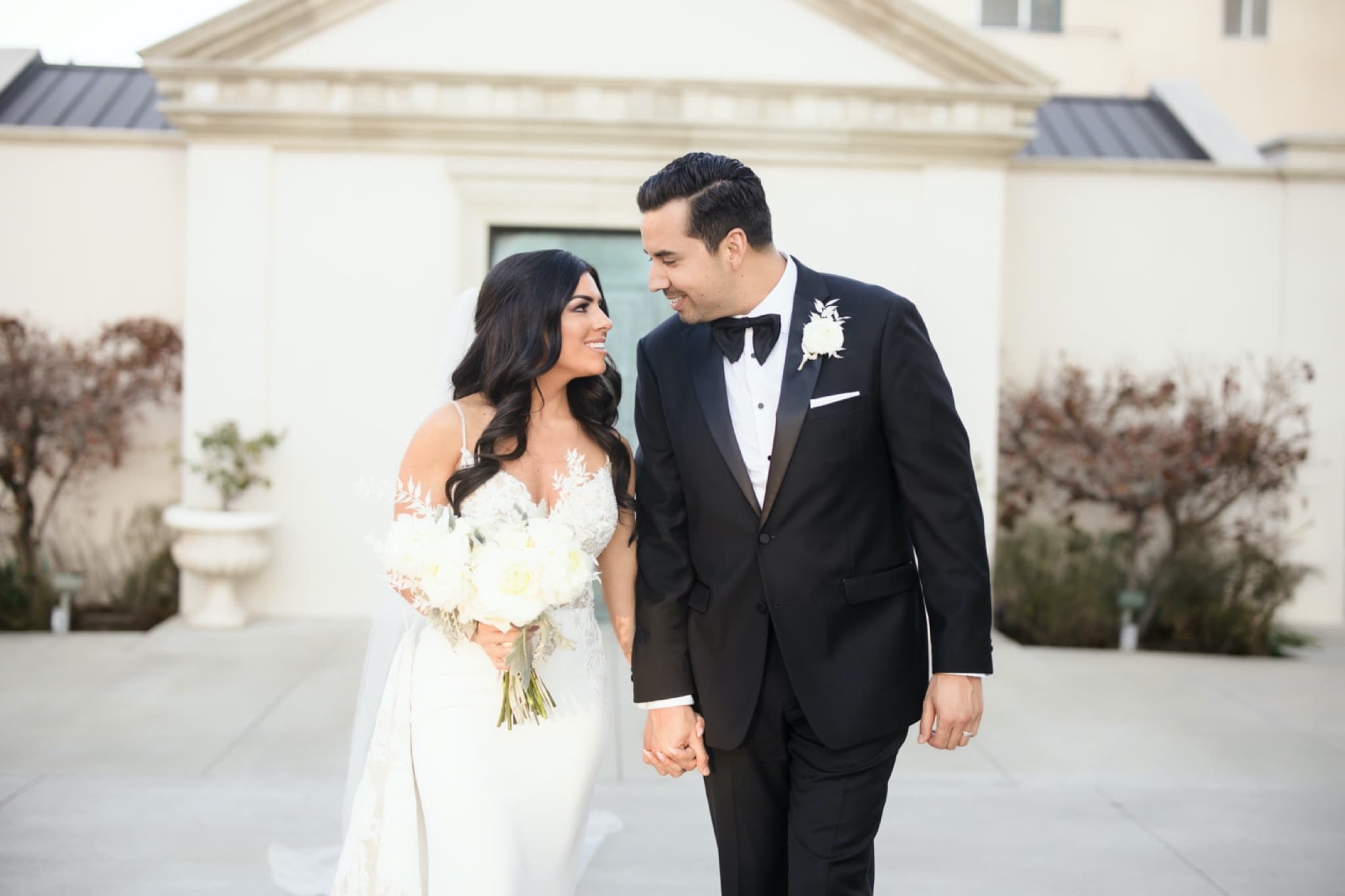 Christina and Ryan laughing hand in hand as they stroll the sunlit courtyard after their cathedral ceremony