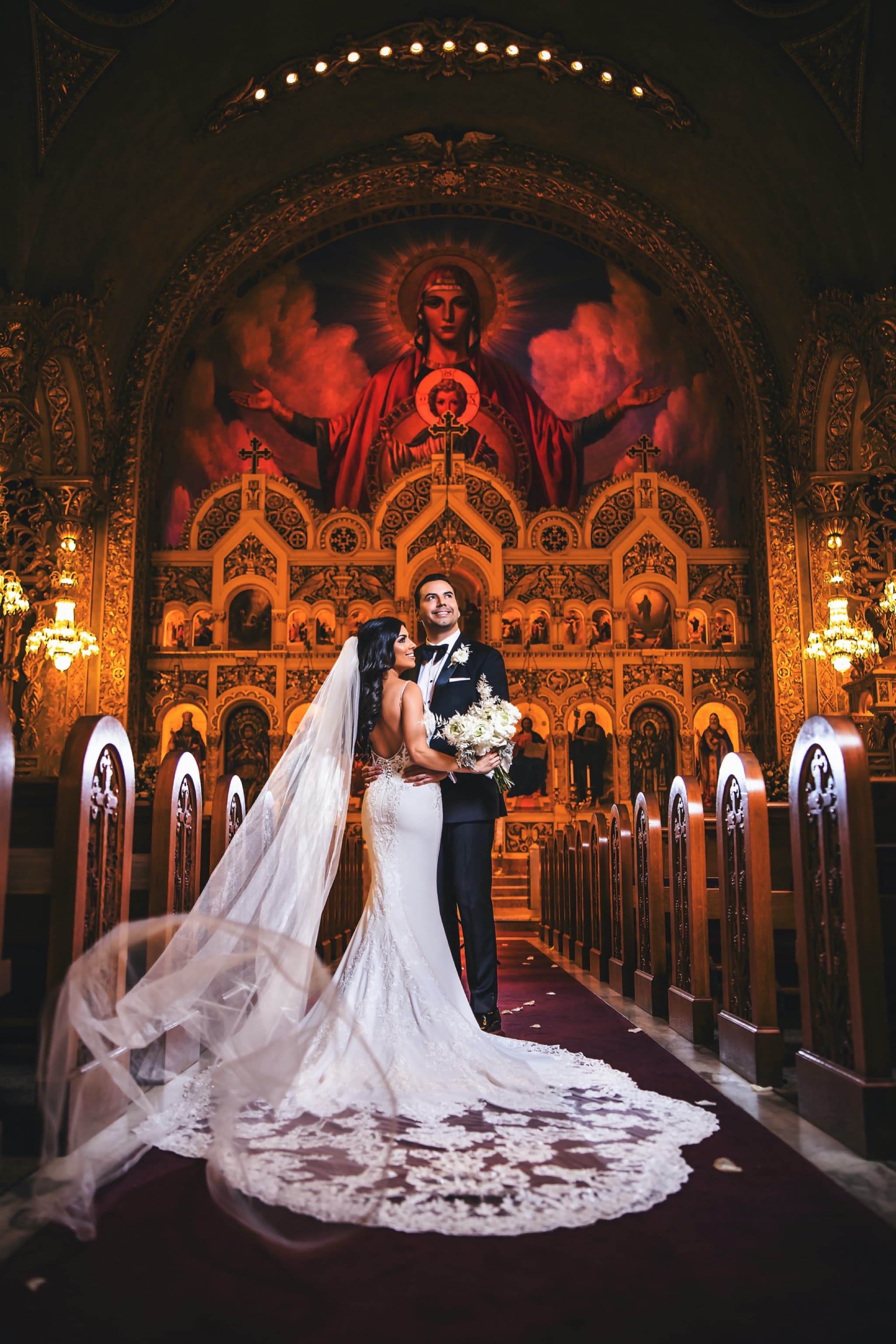 Christina and Ryan on the altar steps of St. Sophia Greek Orthodox Cathedral, her lace veil spread down the crimson aisle beneath the glowing gold Byzantine sanctuary, photographed by Michael Anthony Photography
