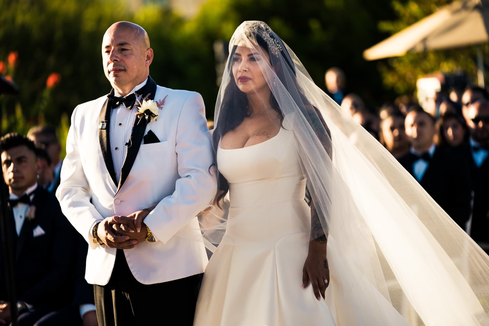 Elise and Luis standing together during their ceremony, her cathedral veil catching the ocean breeze
