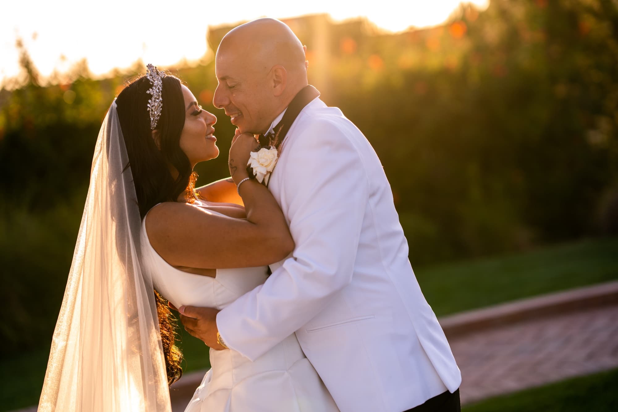 Elise and Luis embracing in the golden-hour light with the sun flaring through the grasses at Terranea