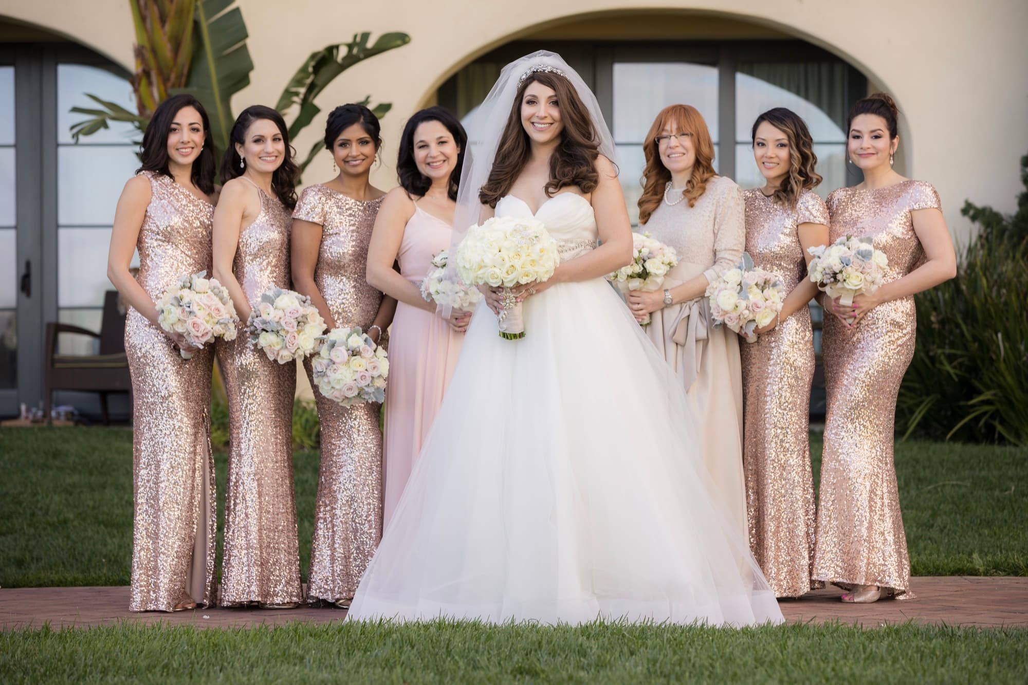 Bride with her bridesmaids in gold sequin gowns holding ivory bouquets on the lawn at Terranea Resort