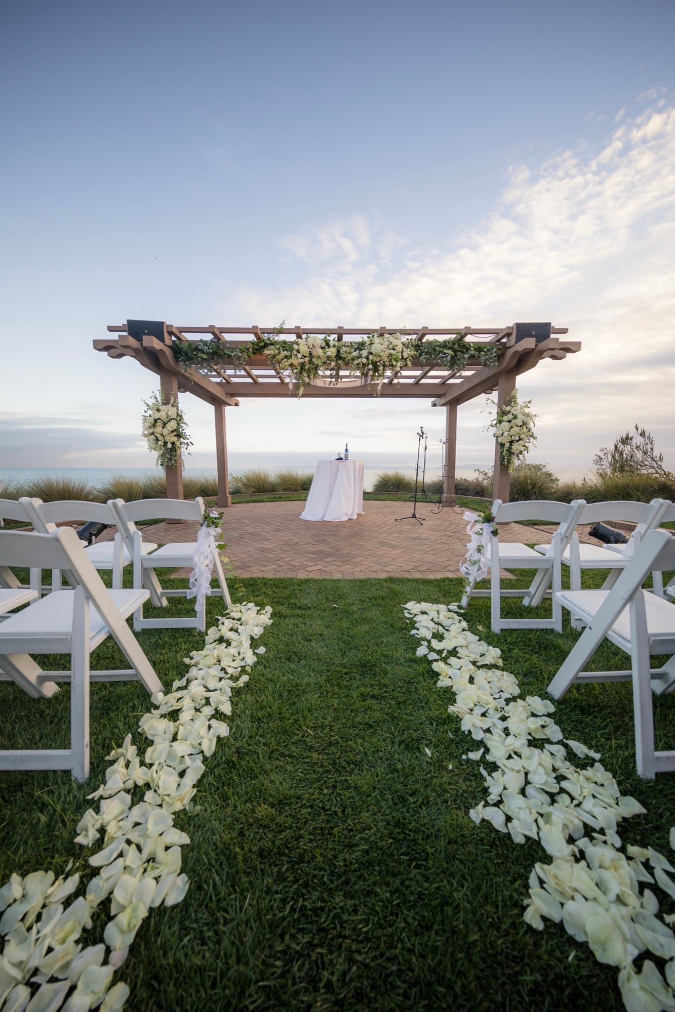 Empty chuppah pergola with white rose petals lining the grass aisle before a dusk wedding ceremony at Terranea Resort