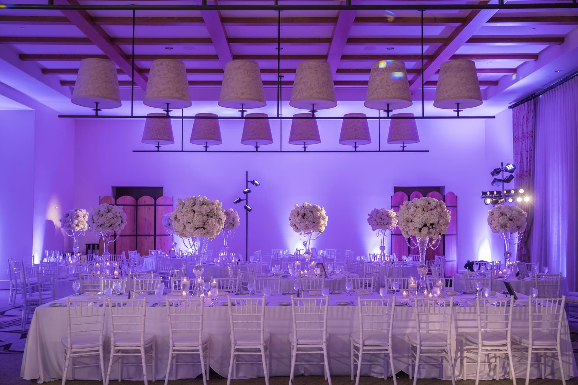 Terranea Resort ballroom lit in violet with tall white floral centerpieces and candlelight before the wedding reception