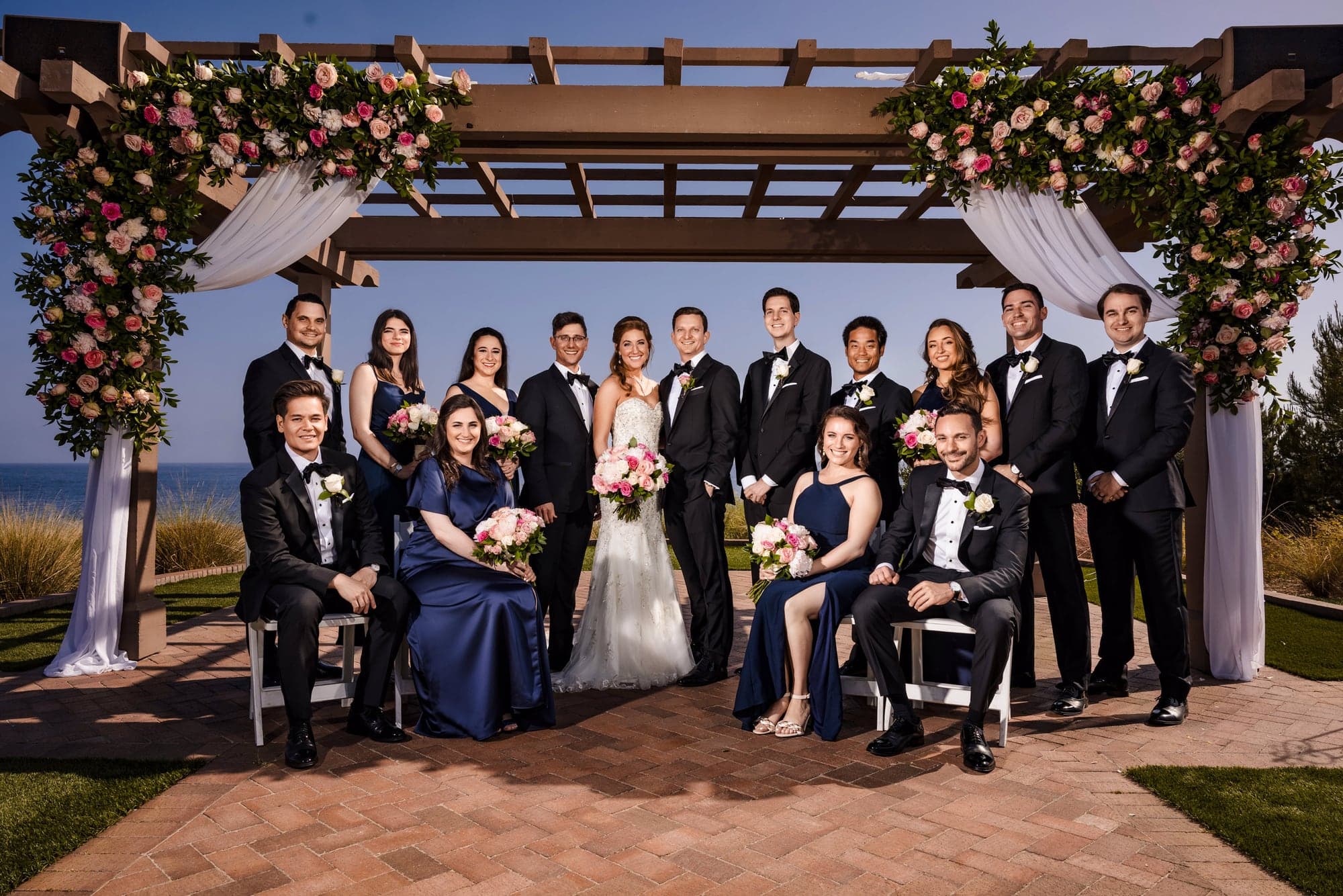 Sarah and Daniel with their full wedding party beneath a floral pergola at Terranea Resort