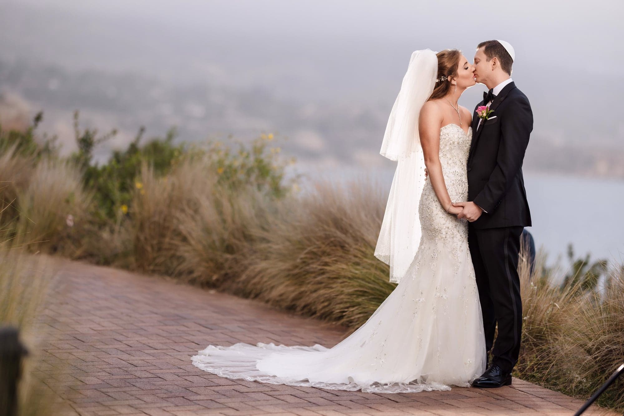 Sarah and Daniel embracing in the coastal grass above the Pacific at Terranea Resort