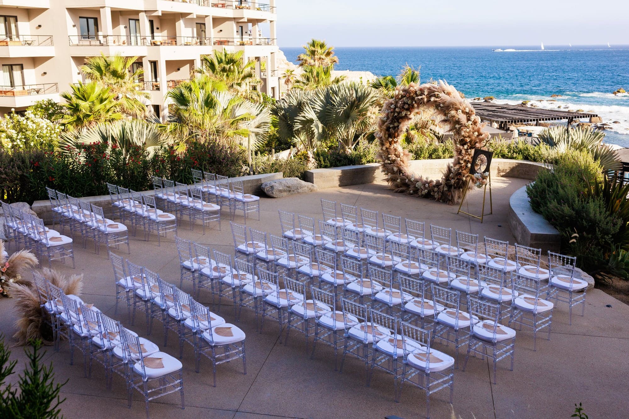 The oceanfront ceremony terrace at The Cape Cabo prepared with white chairs and a circular floral arch