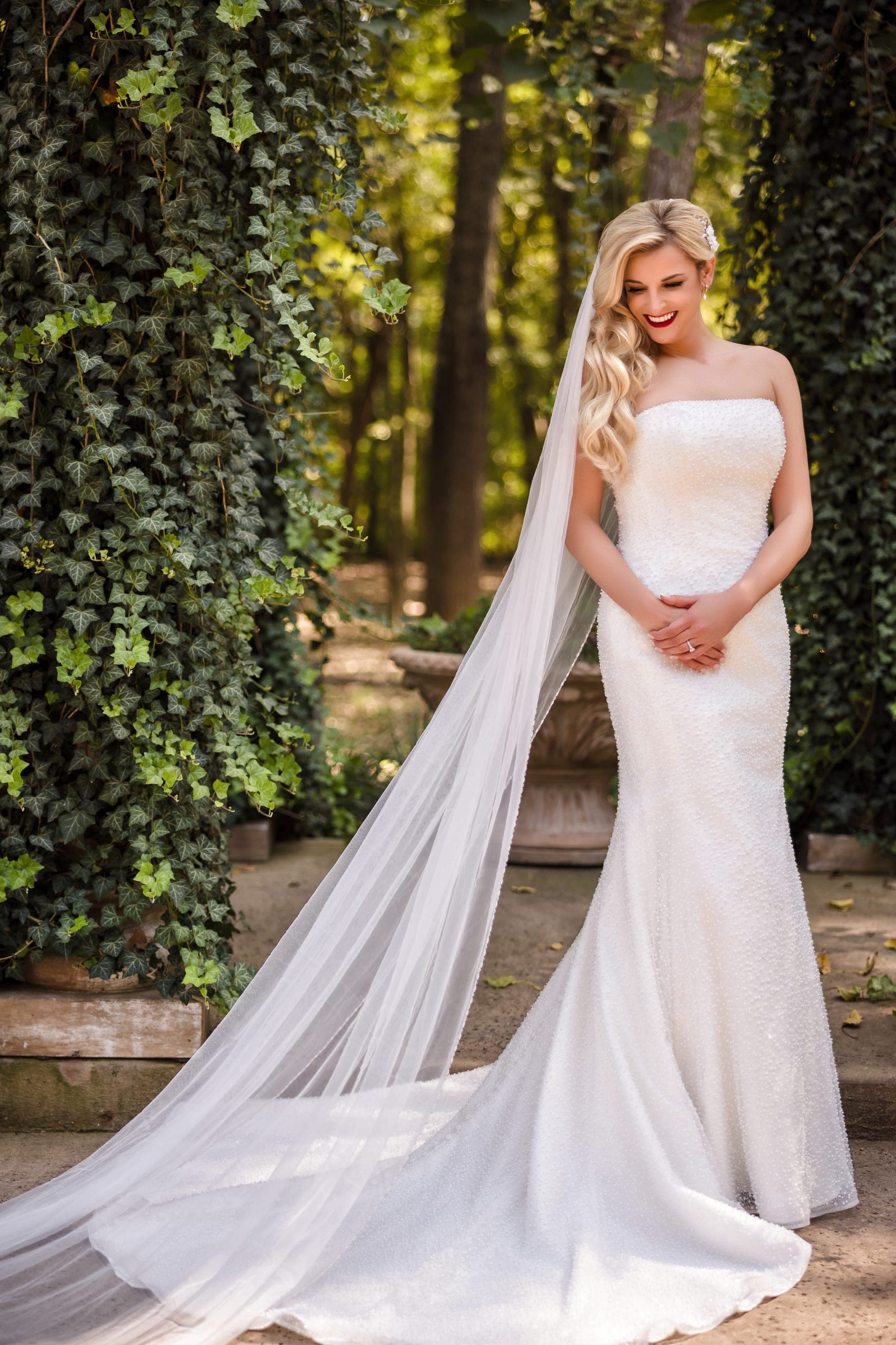 Bridal portrait of Beth in her fitted gown and cathedral veil against a wall of ivy