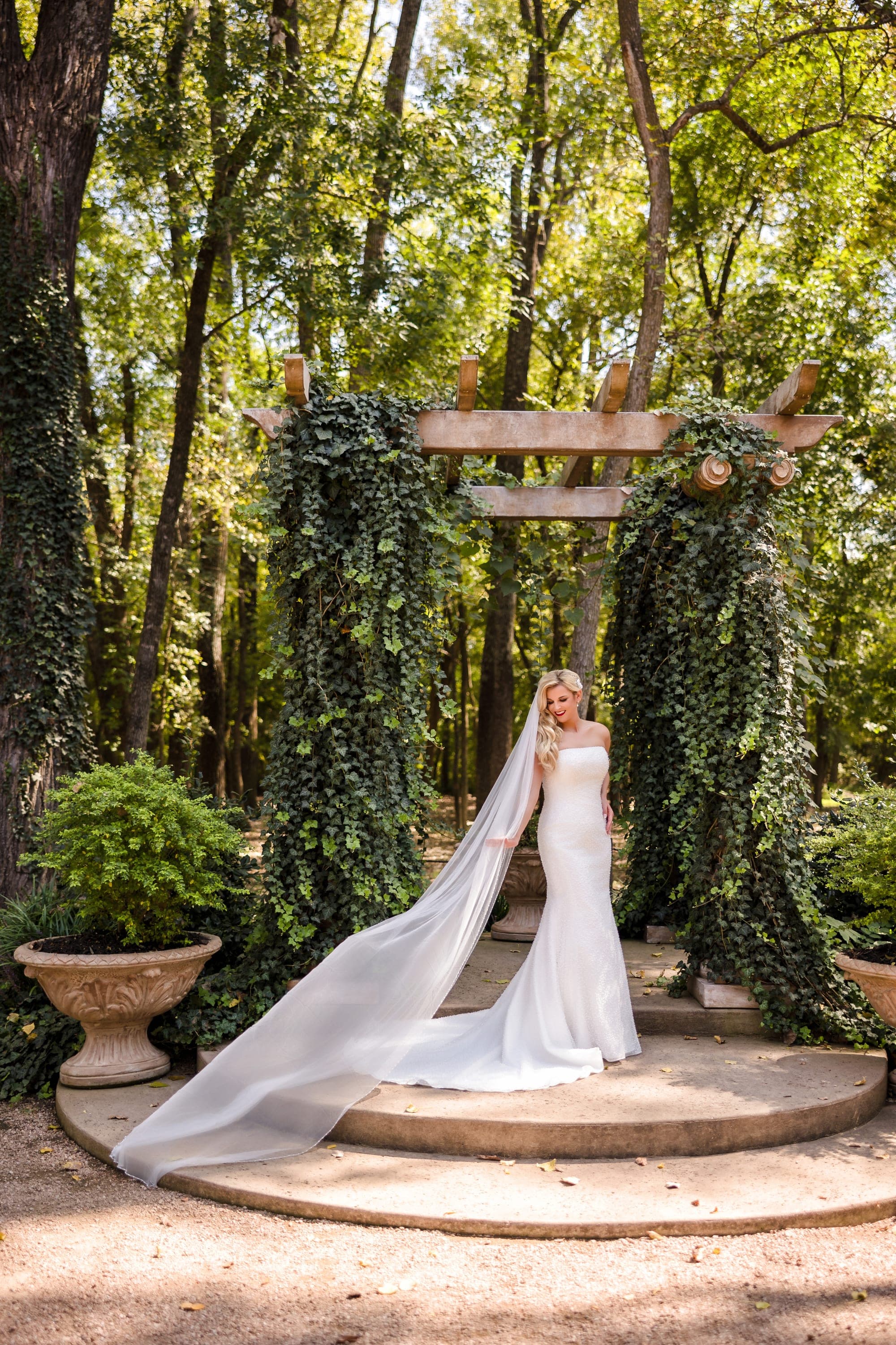 Beth's cathedral veil trailing across the stone steps beneath the greenery-covered arch