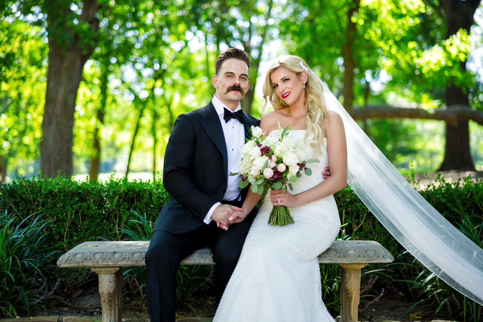 The couple seated together on a stone bench under the trees at The Springs