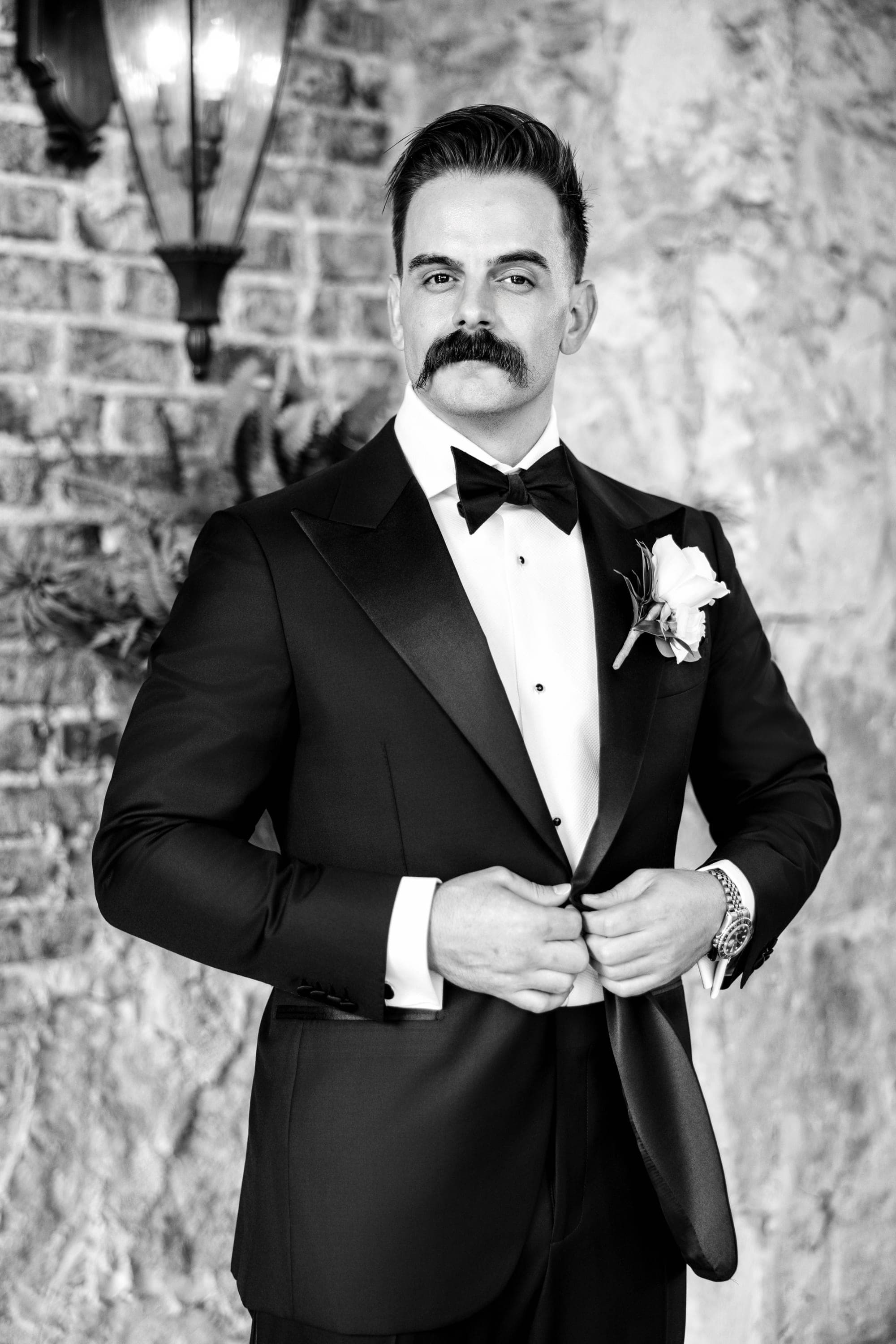 Black and white portrait of Austin in his tuxedo against a brick wall