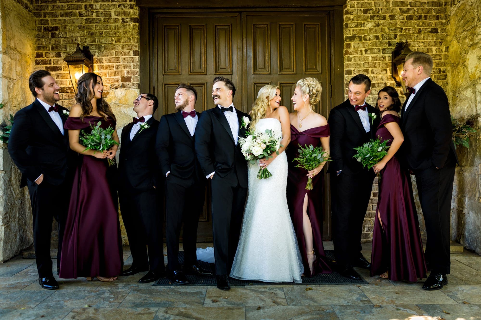 The full wedding party, groomsmen in black tuxedos and bridesmaids in burgundy