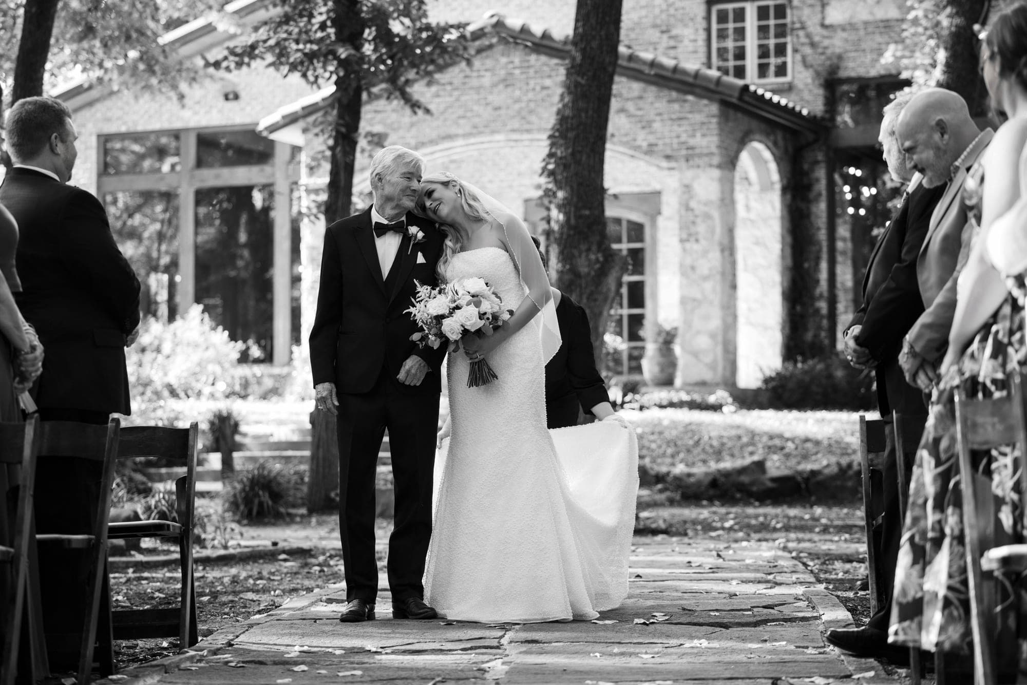 Beth walking down the outdoor aisle on her father's arm as guests stand