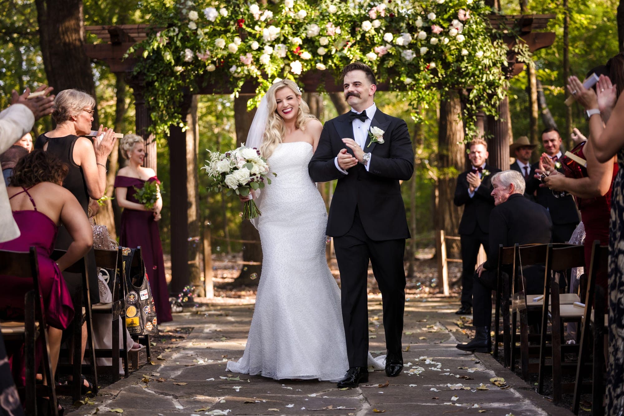The ceremony beneath the greenery-covered pergola surrounded by tall trees