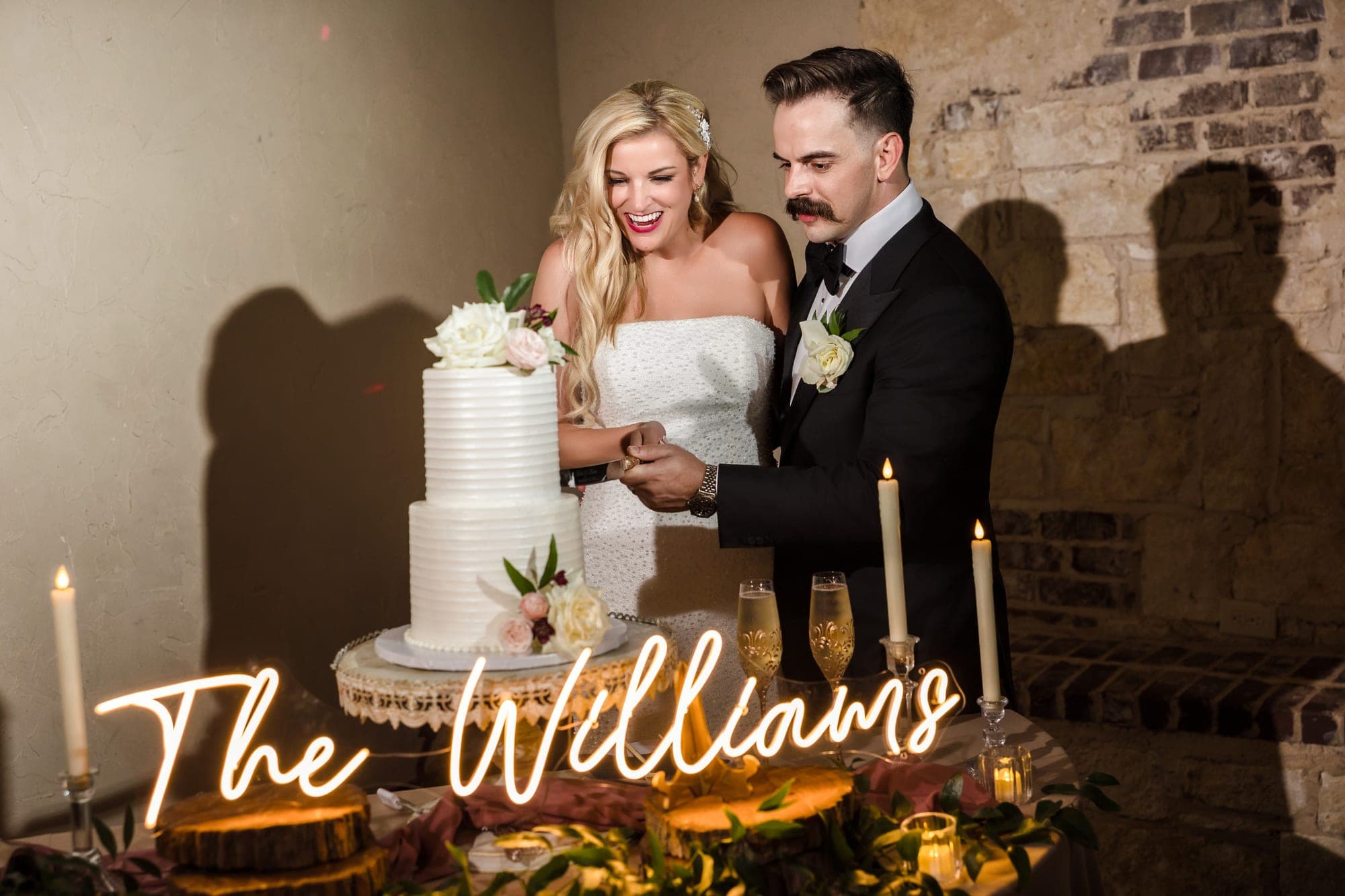 Beth and Austin cutting their cake beneath a neon sign reading The Williams