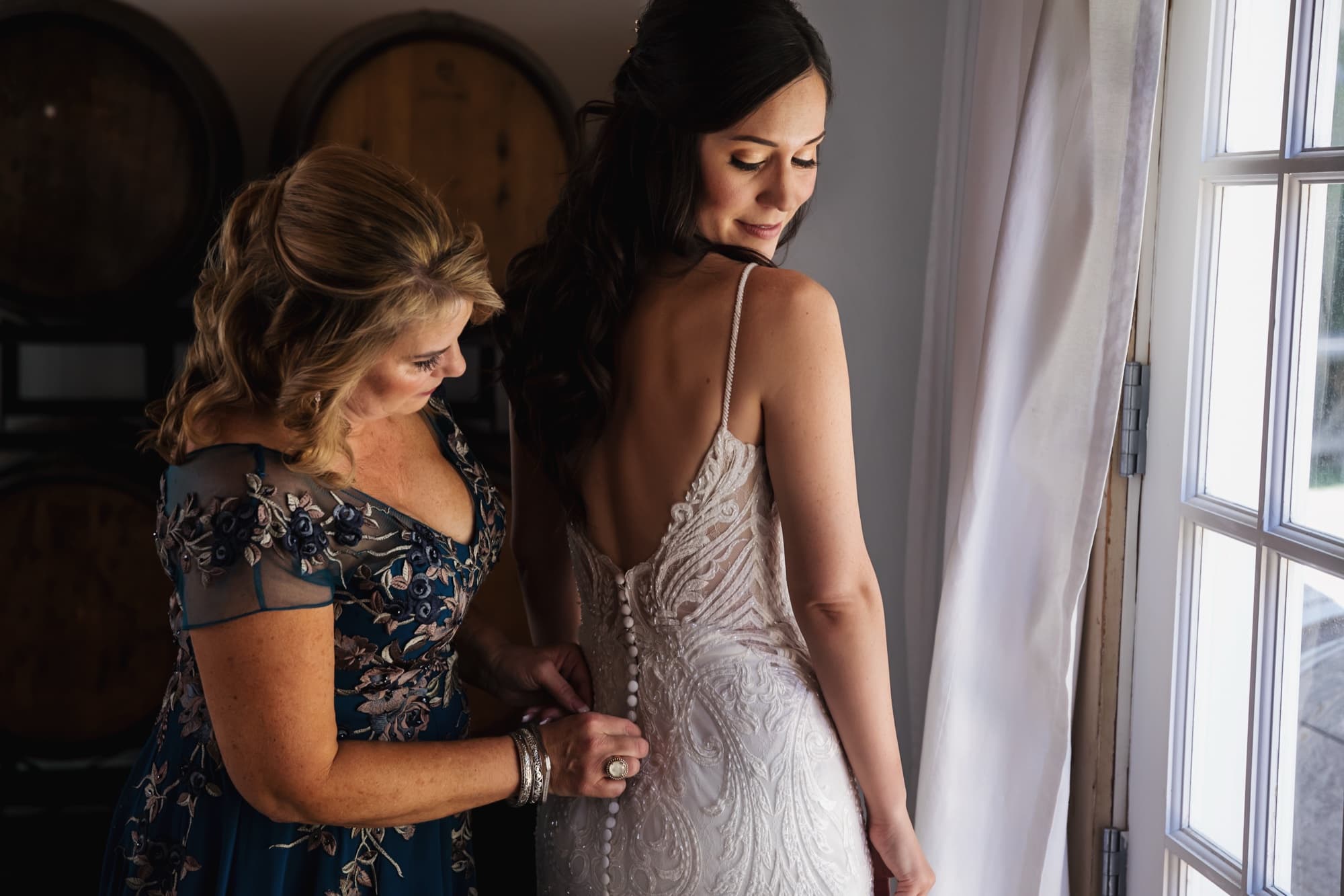 Allison's mother buttoning the back of her lace gown in the window light of the barn