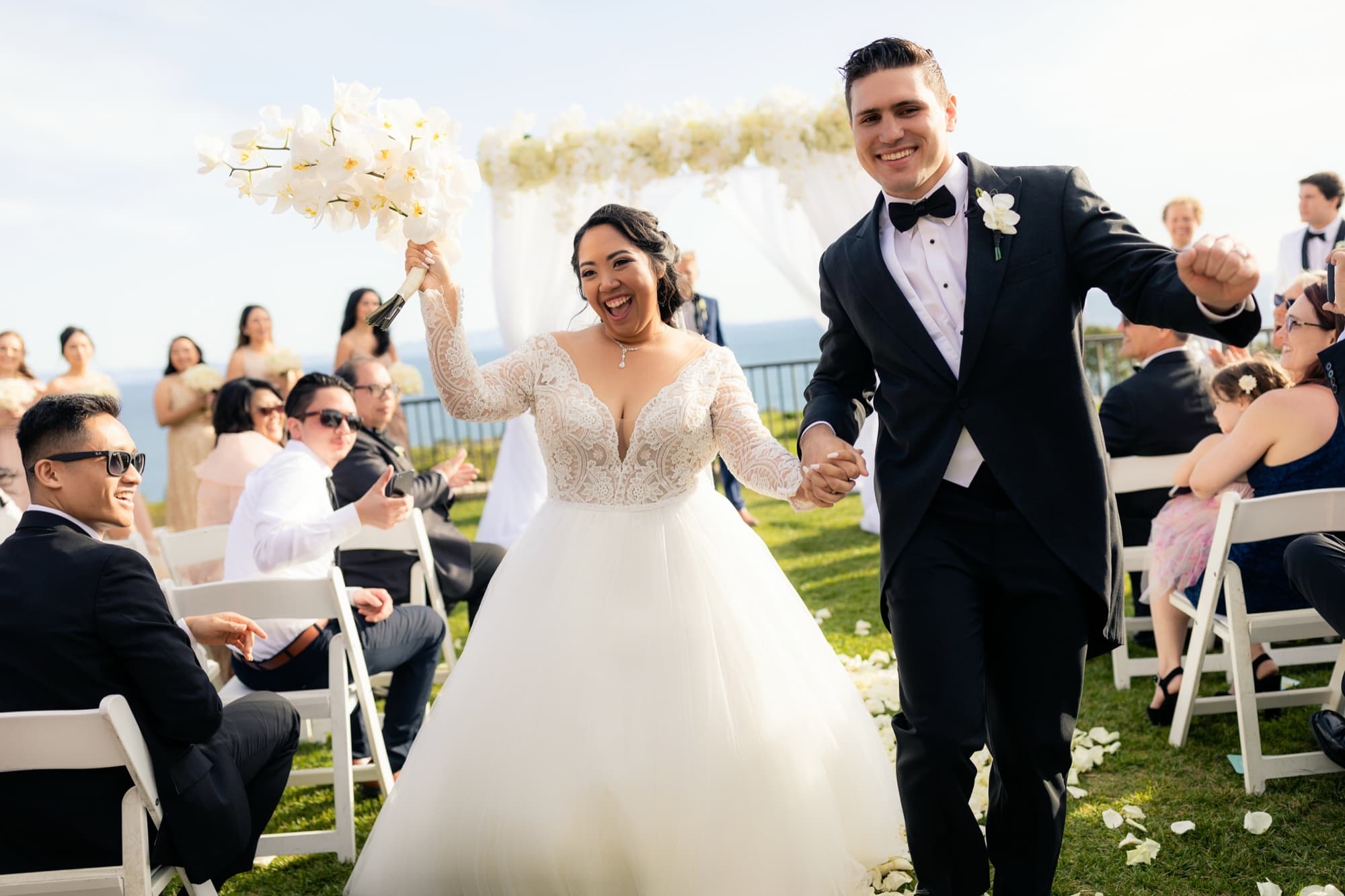Jamie and James laughing hand in hand as they recess up the petal-covered aisle past cheering guests