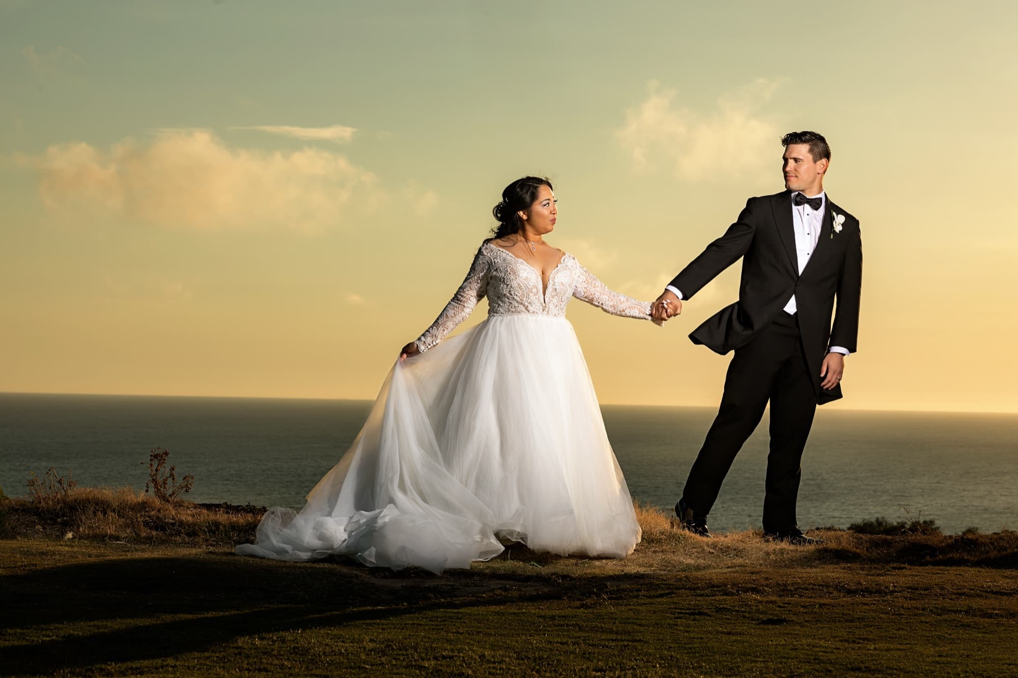 Jamie and James strolling hand in hand across the golden clifftop at sunset, the dark Pacific stretching behind them