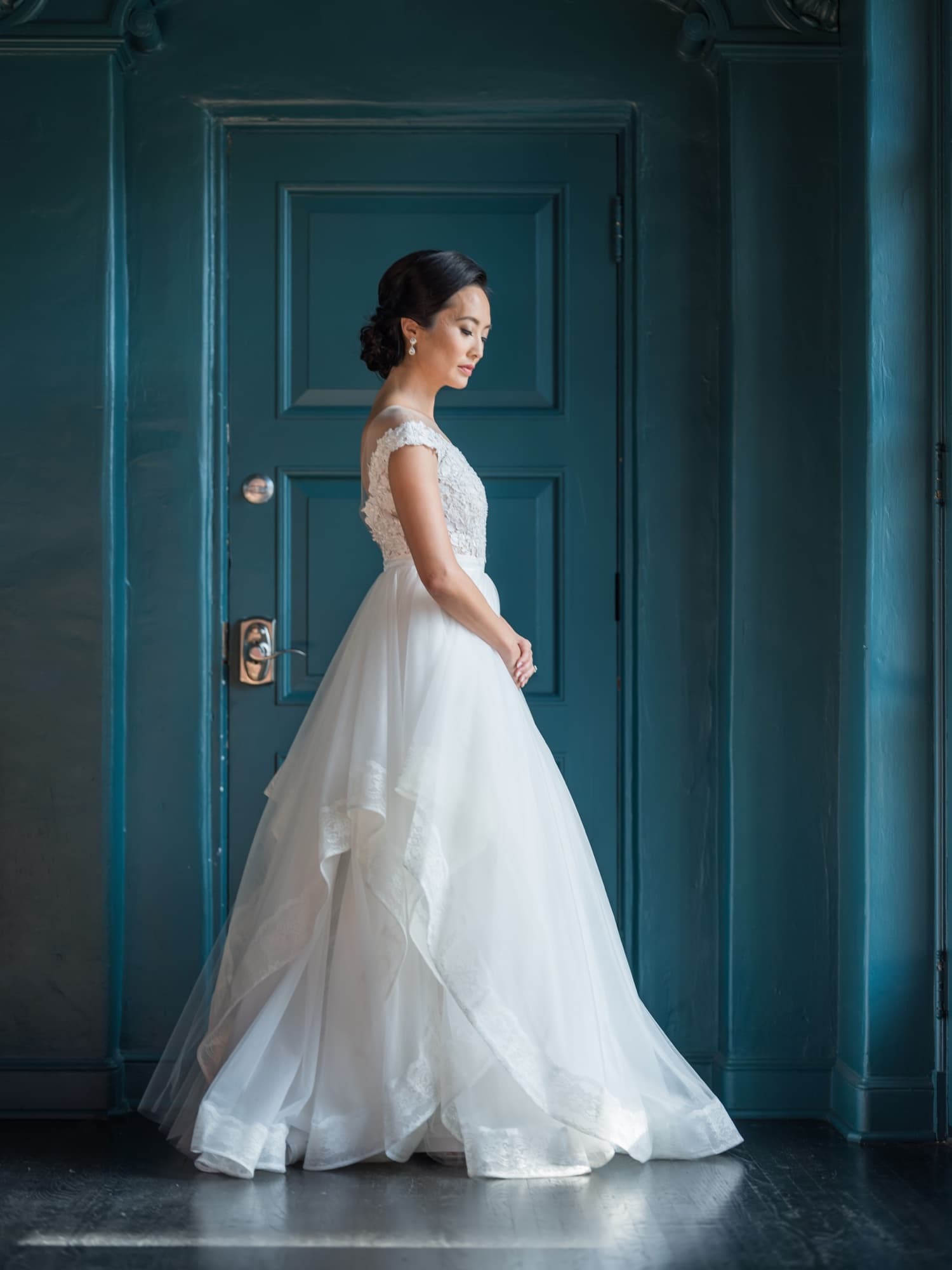 Bride in a layered tulle ball gown standing in profile against the deep teal doors of the Vibiana bridal suite