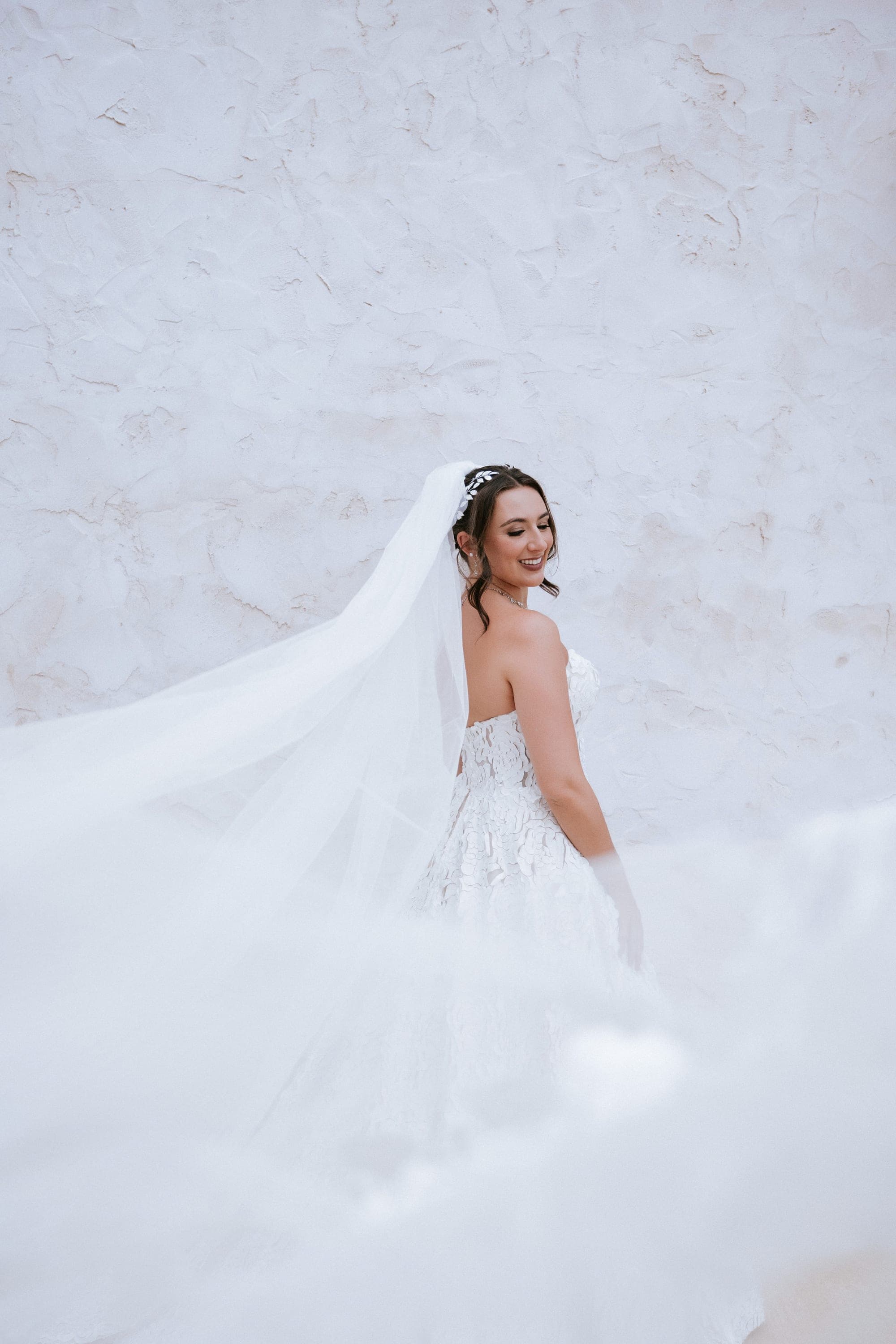 Full-length bridal portrait against the villa's white plaster wall, veil and train swept wide