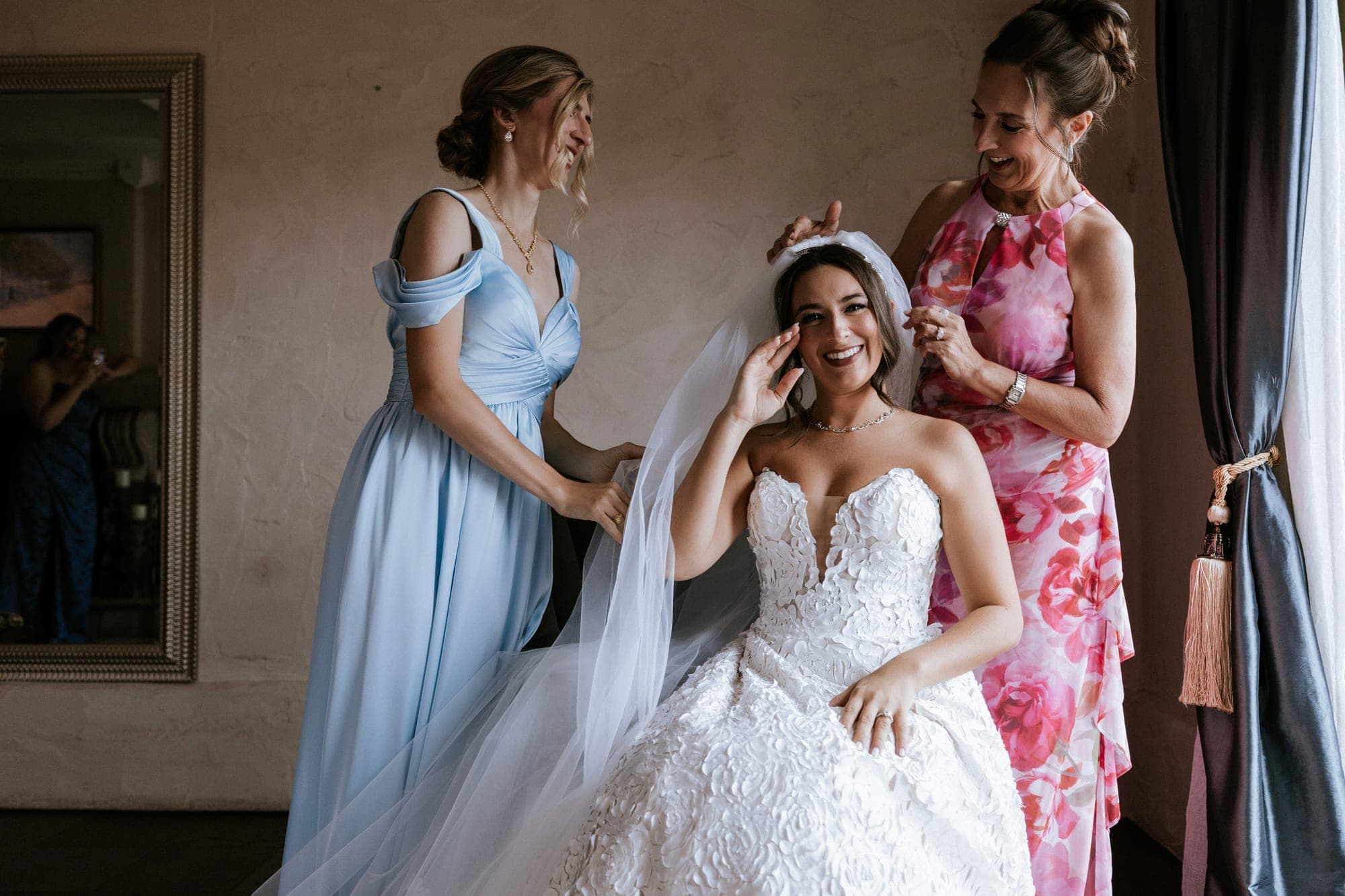 Kelsey laughing as her mother and bridesmaid set her cathedral veil